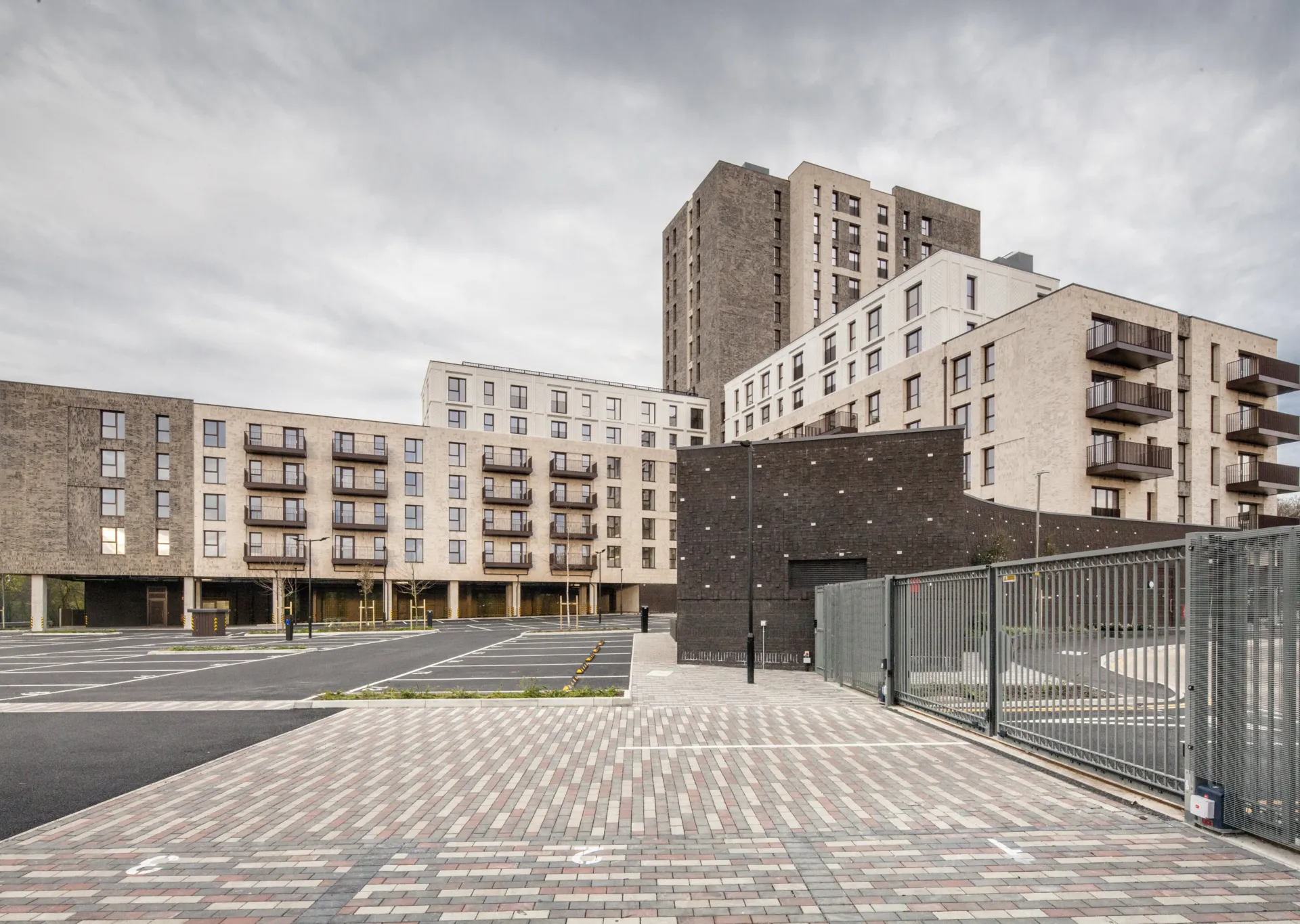 A modern residential building with different numbers of storeys in different parts. Balconies are shown and patterned brick paving is in the foreground.