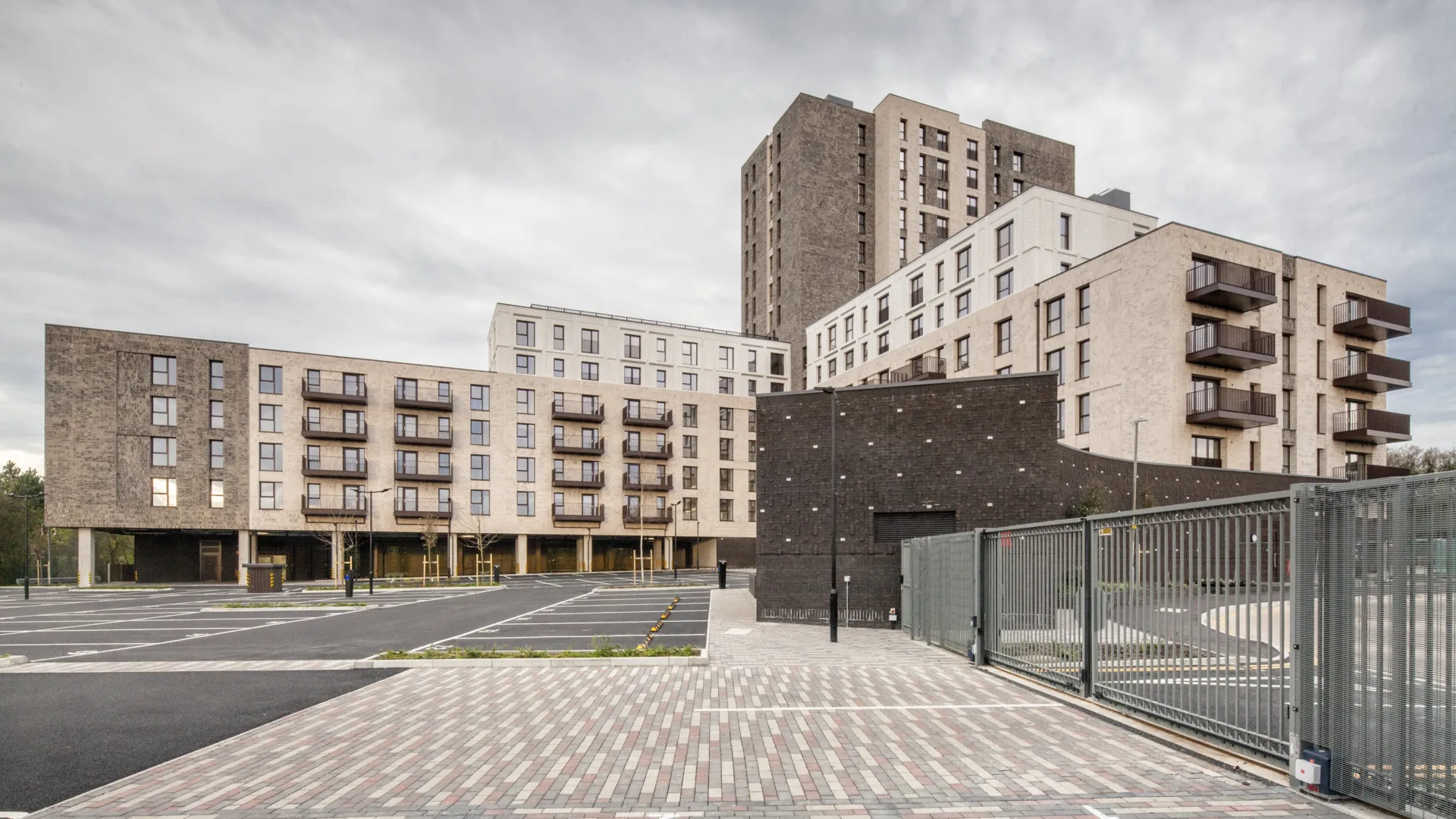 A modern residential building with different numbers of storeys in different parts. Balconies are shown and patterned brick paving is in the foreground.