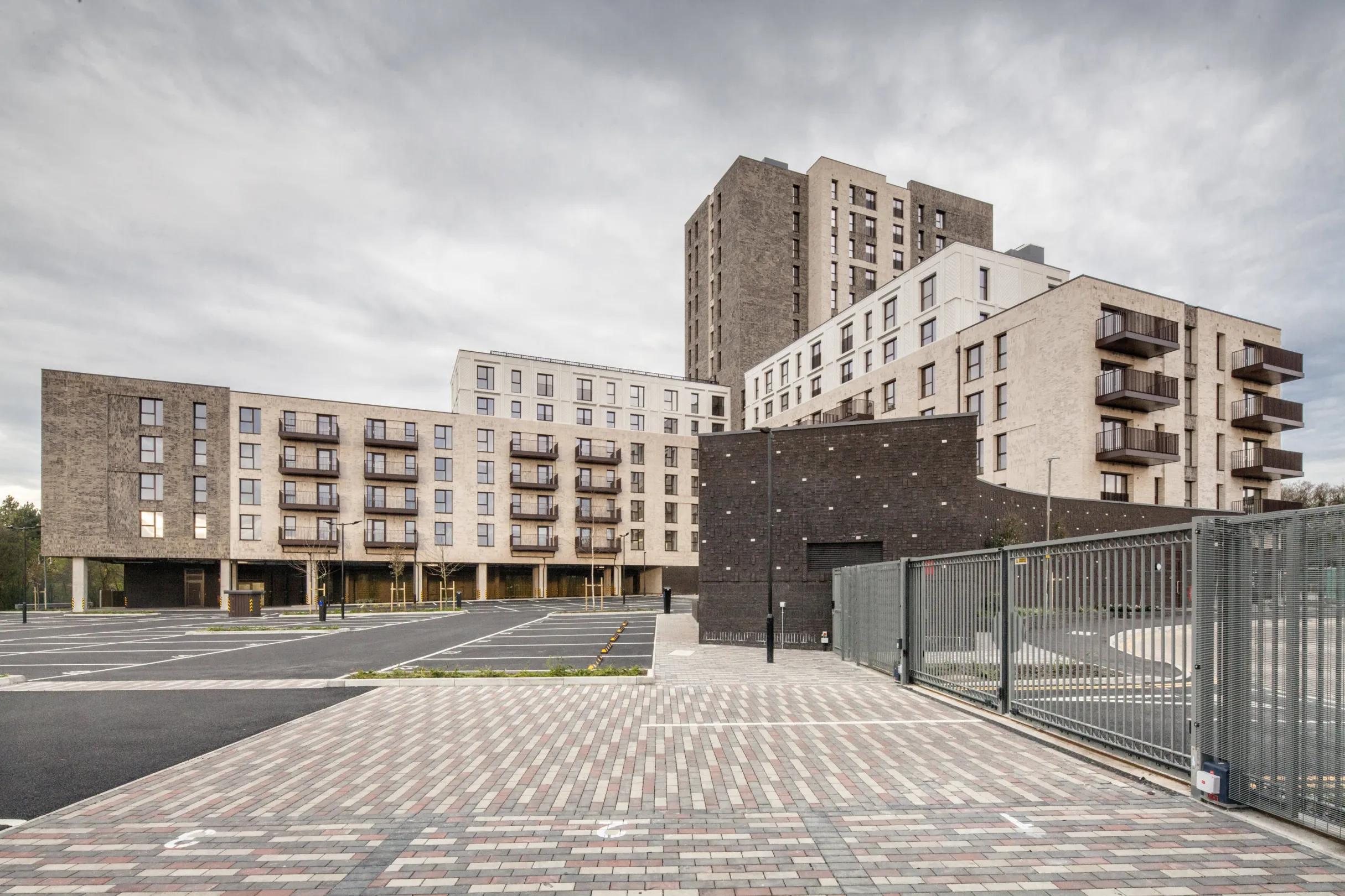 A modern residential building with different numbers of storeys in different parts. Balconies are shown and patterned brick paving is in the foreground.