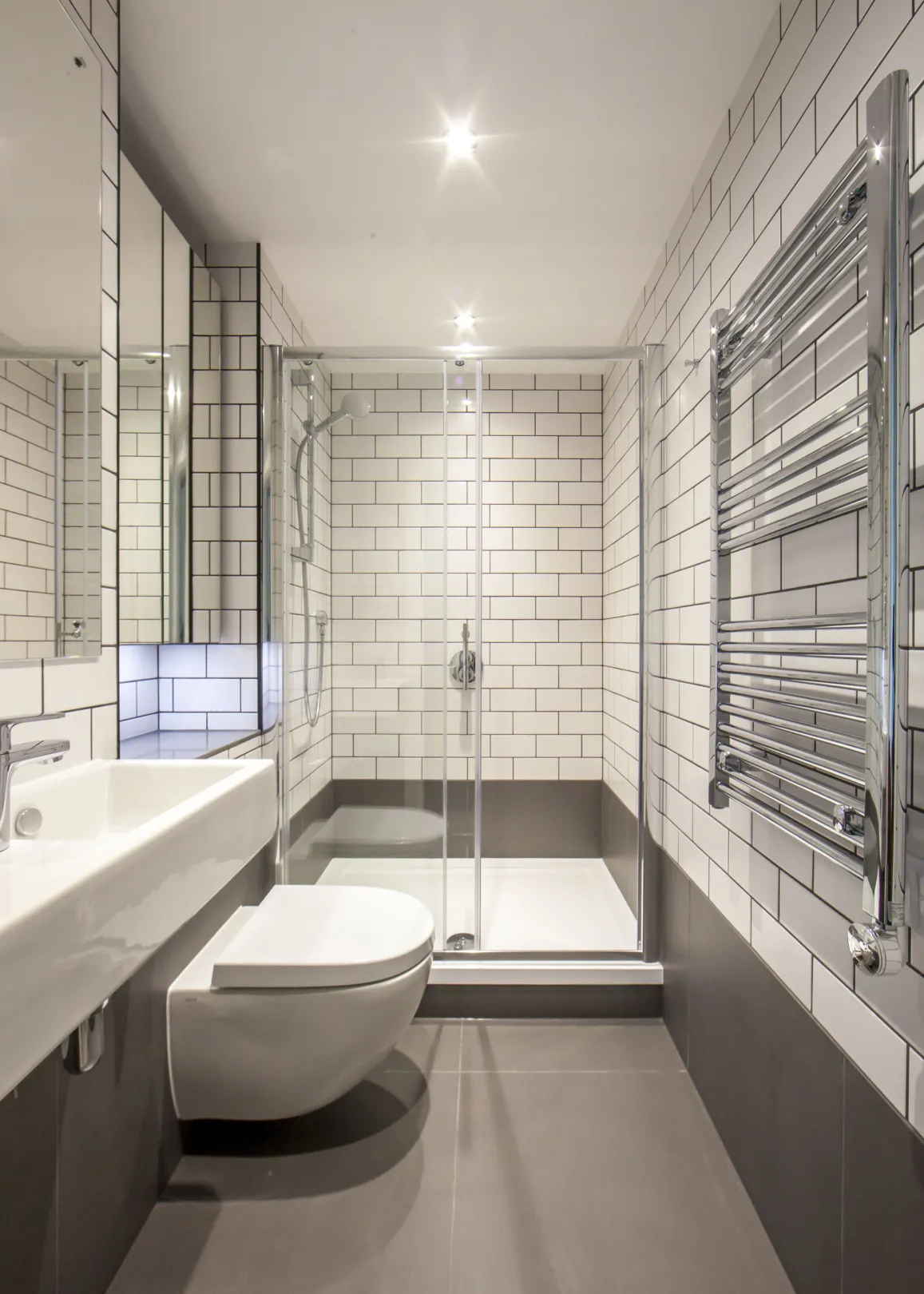 A modern bathroom with shower, large mirror and chrome heated towel radiator.
