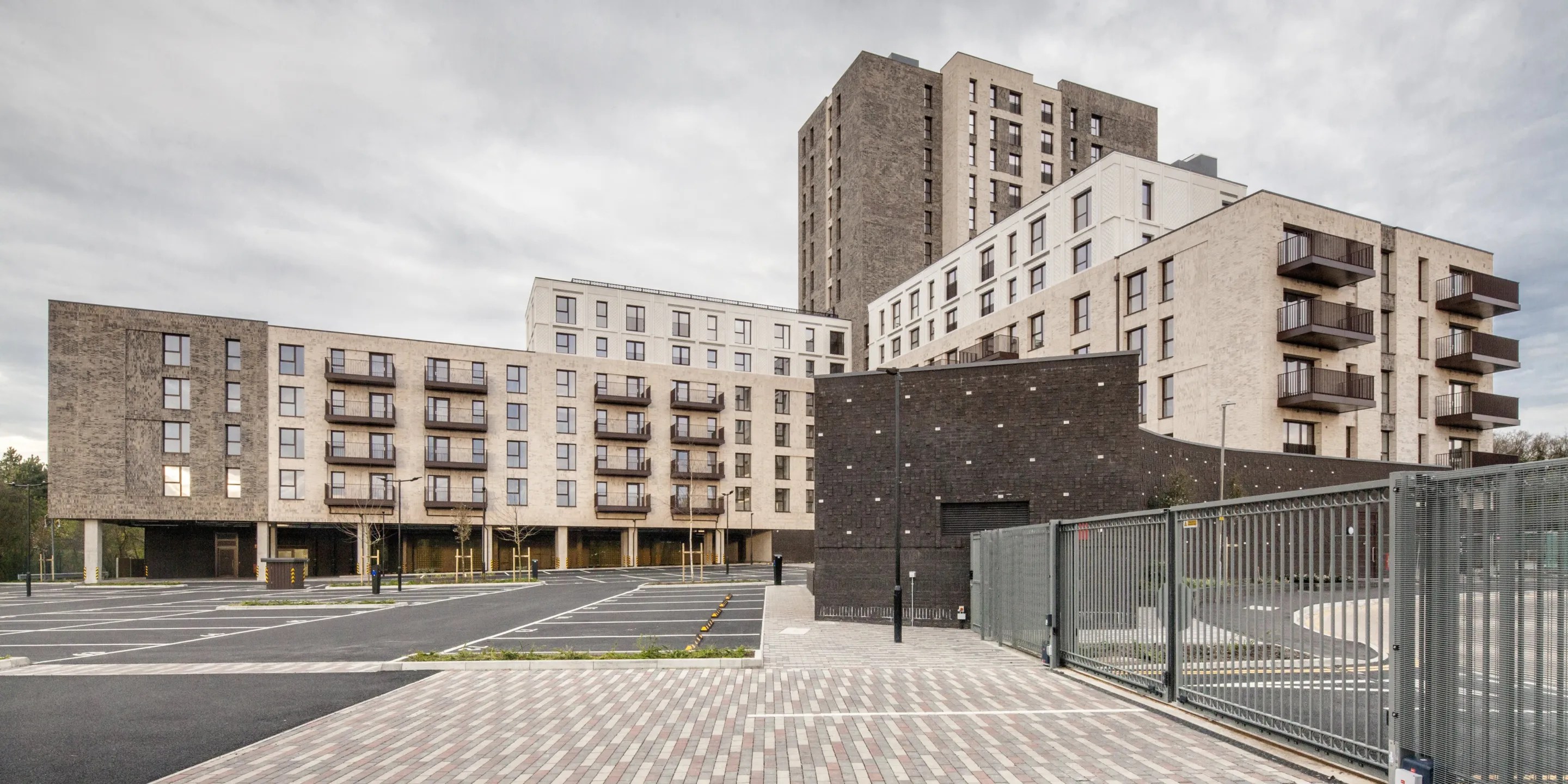 A modern residential building with different numbers of storeys in different parts. Balconies are shown and patterned brick paving is in the foreground.