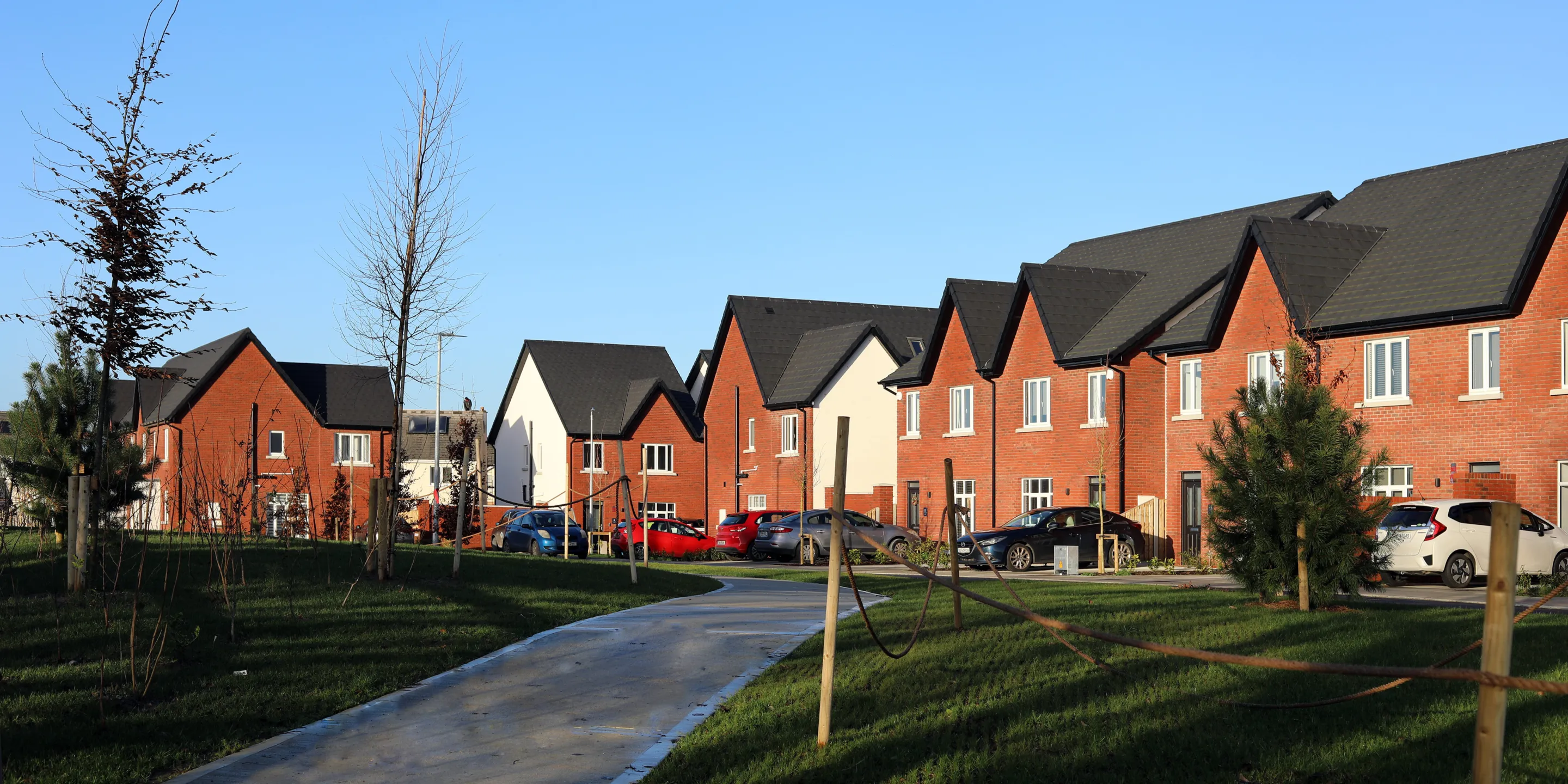 A row of modern red bricked houses, with white PVC windows, pitched roofs and landscaping