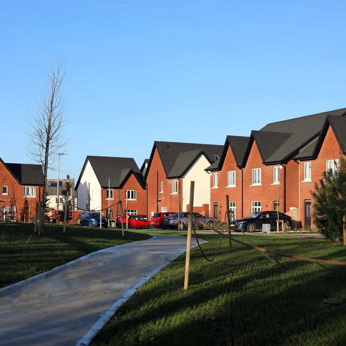 A row of modern red bricked houses, with white PVC windows, pitched roofs and landscaping