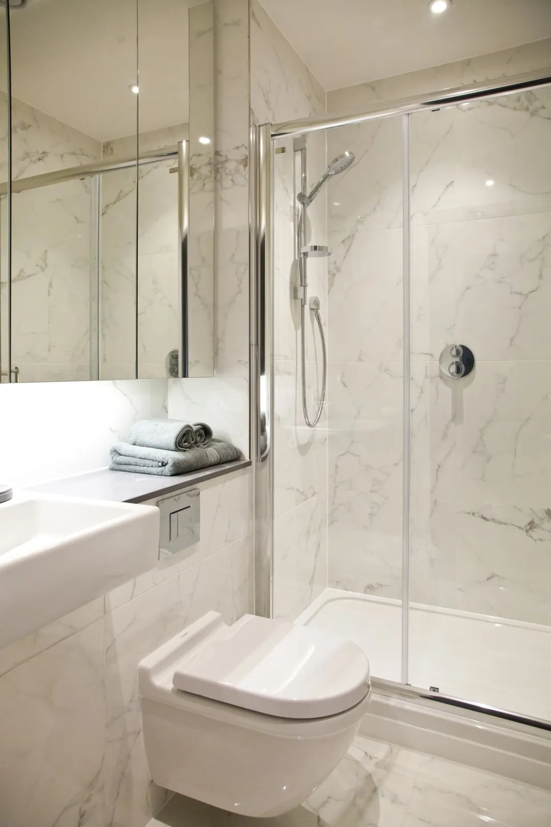 Marble tiled bathroom with large vanity mirror and glass shower screen.