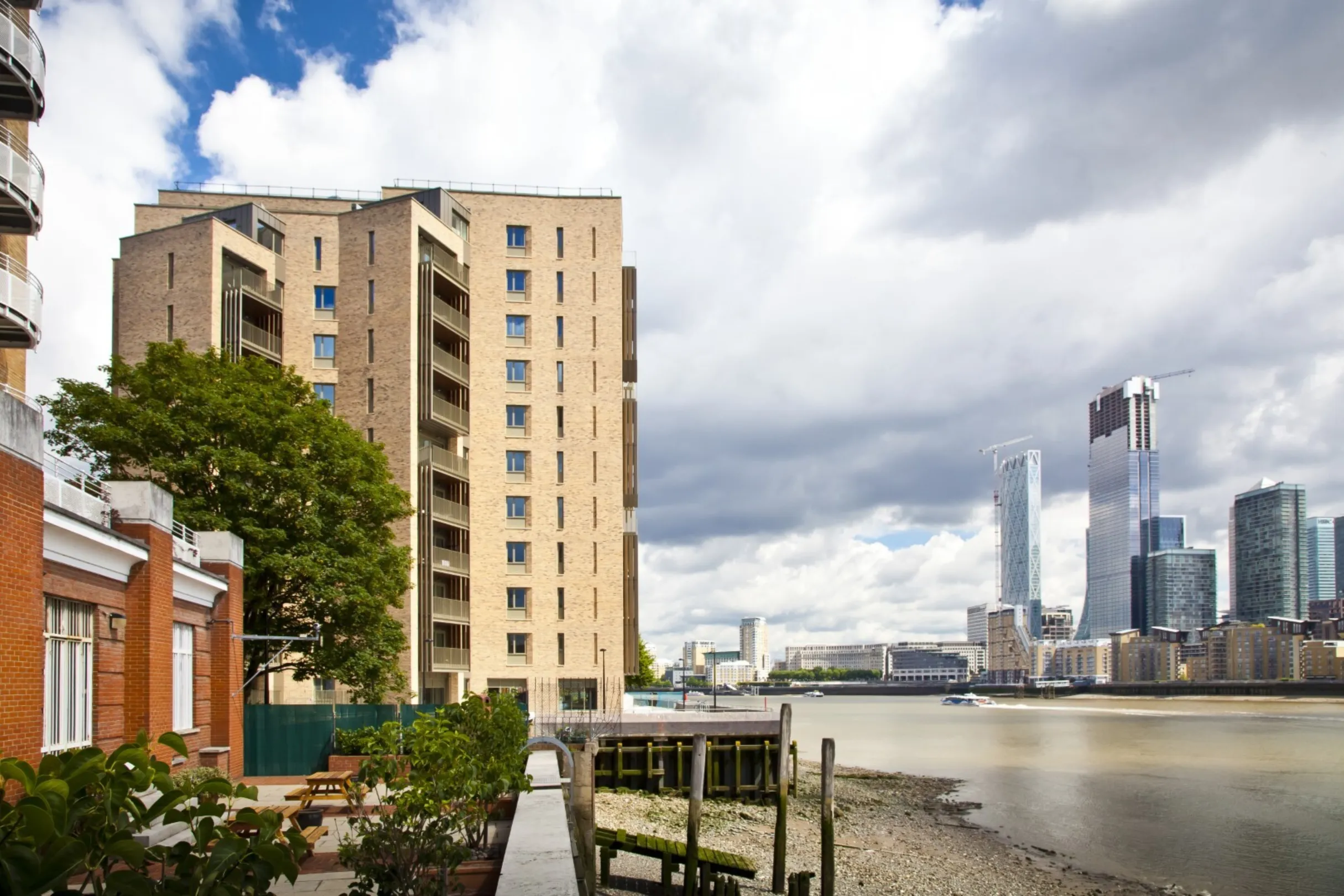Detail of the lower floors of a modern multi storey residential building on the bank of the River Thames. Skyscrapers are visible on the opposite bank.