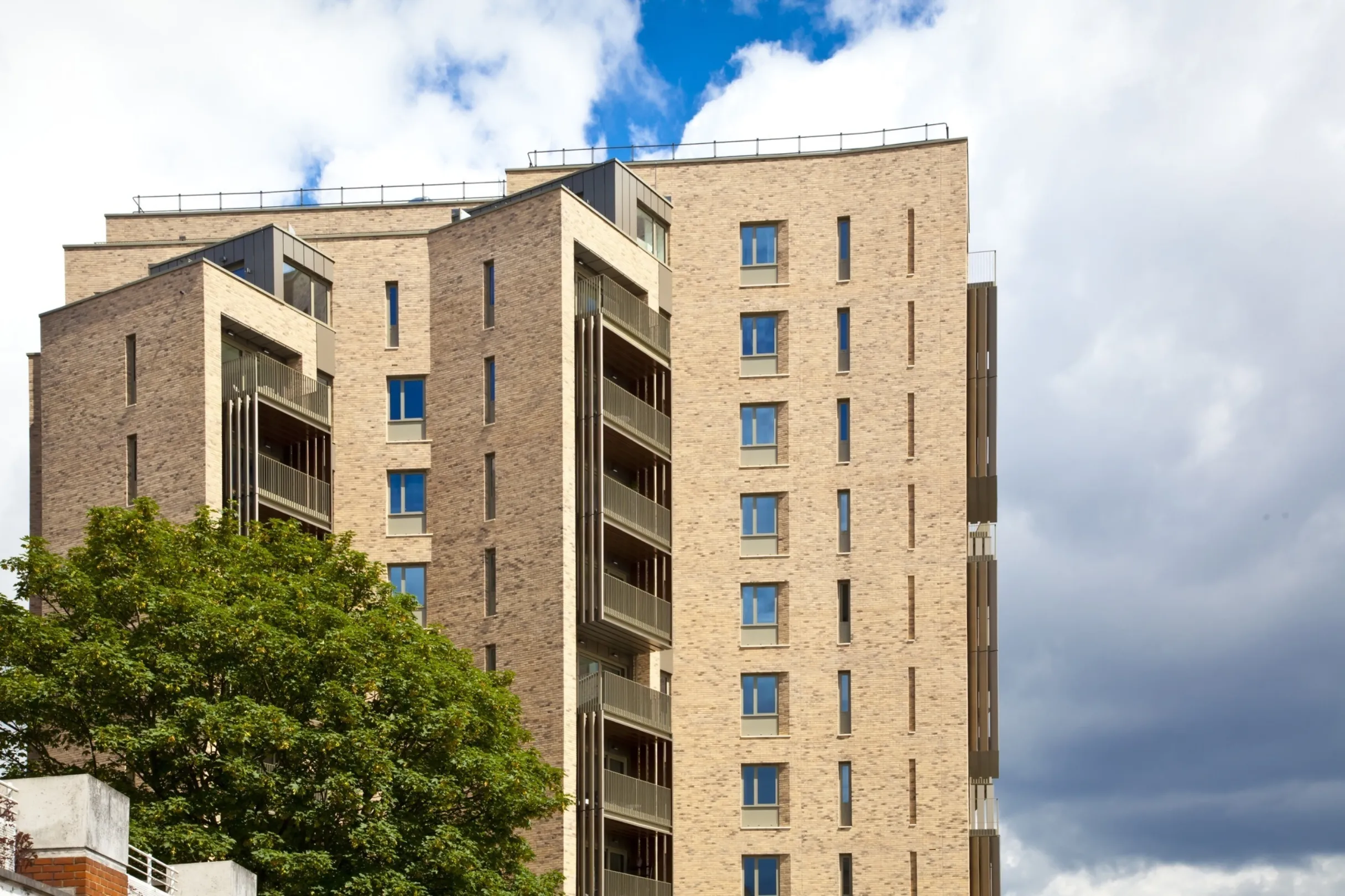 The top section of a modern multi storey residential building with trees in the foreground
