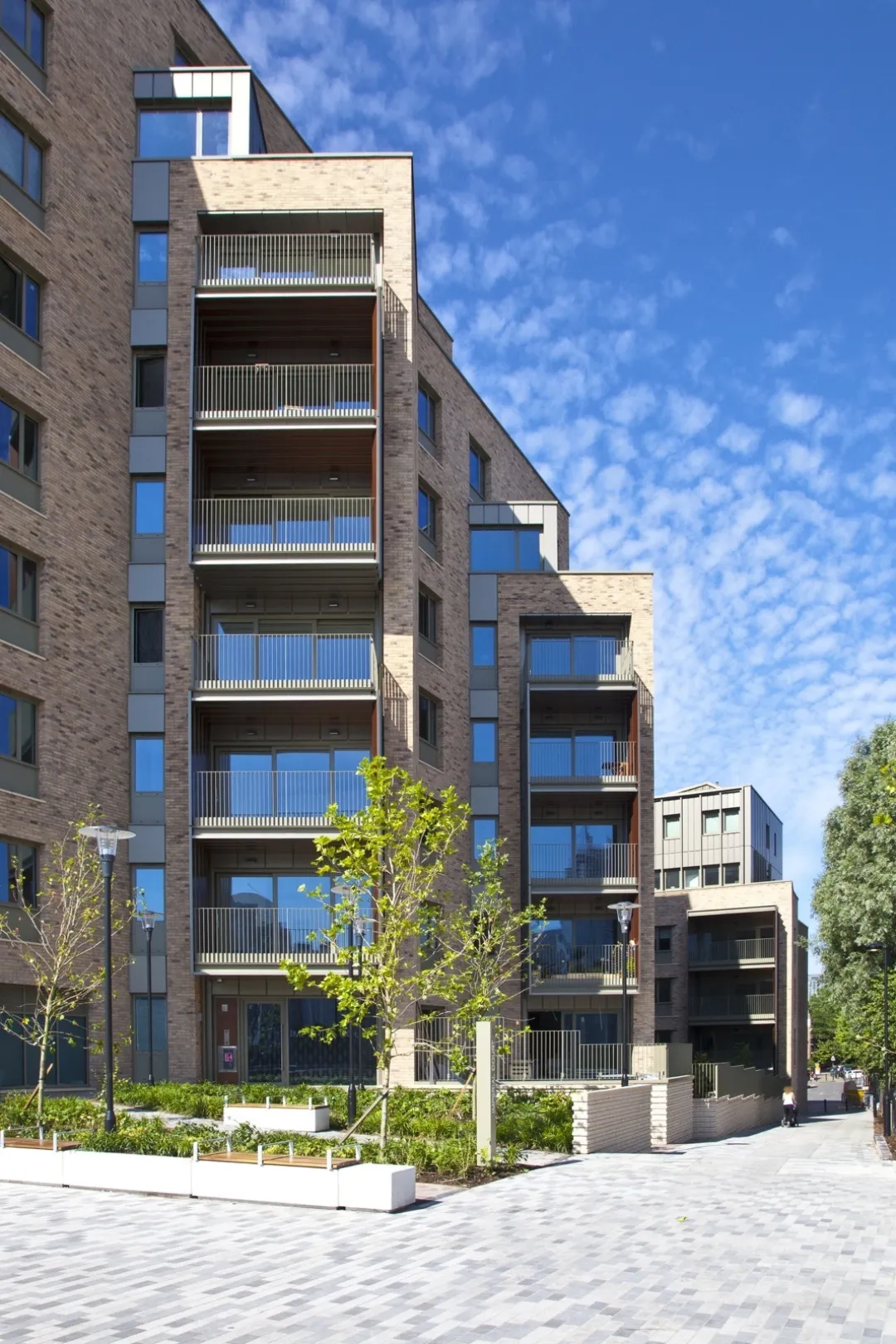 A modern multi storey residential building showing glazing and balconies with landscaped grounds and paved walkway