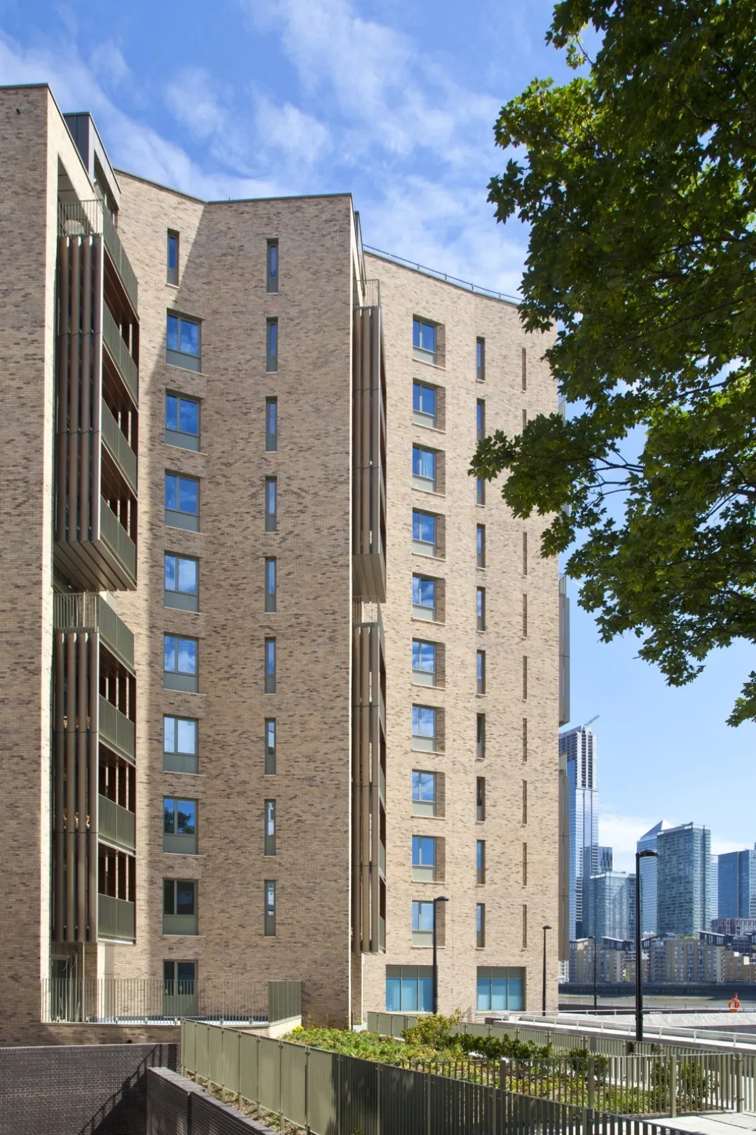 A modern multi storey residential building with trees in the foreground and commercial buildings in the far distance.