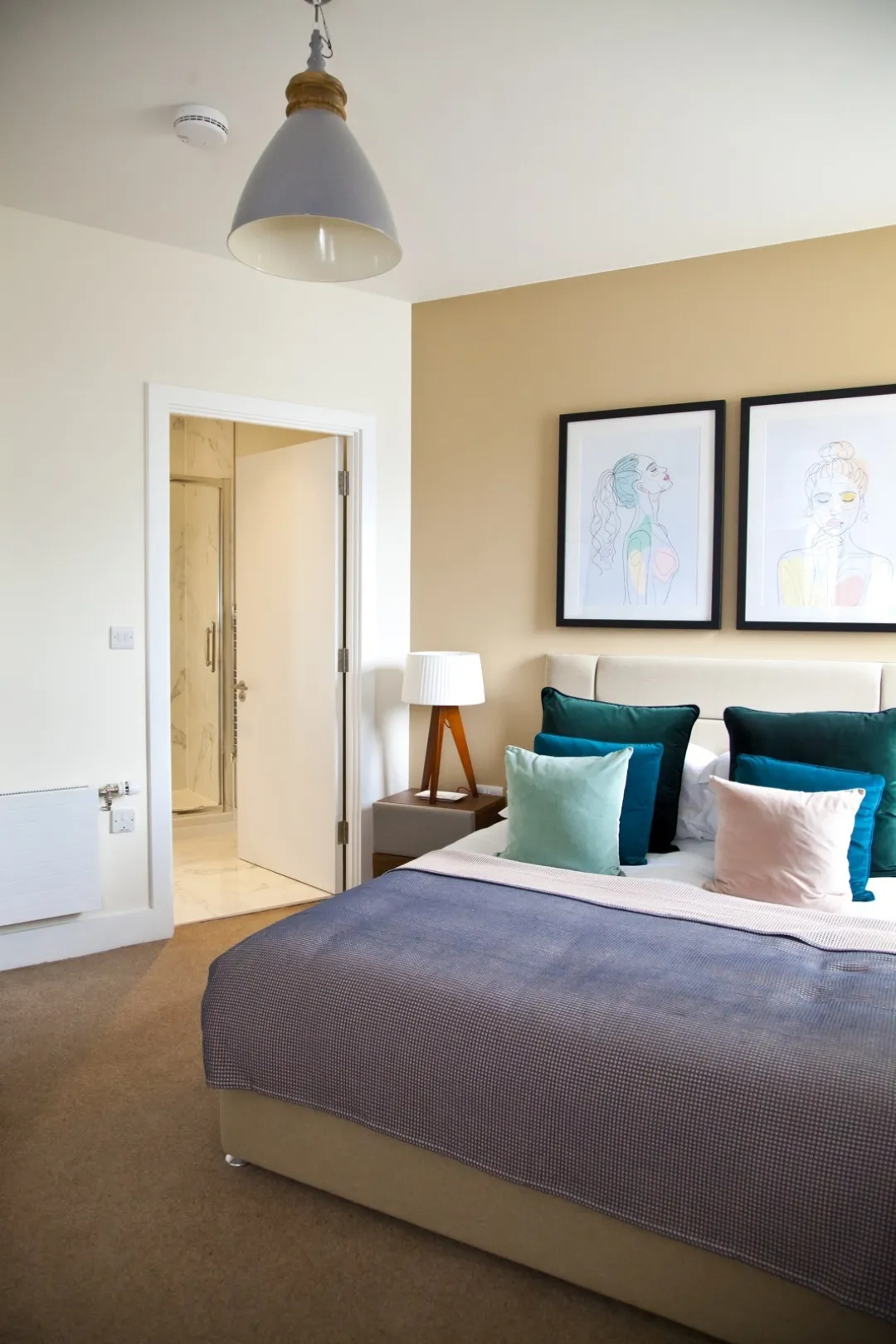 Bedroom of a modern apartment with designer lighting, art on the walls and plush pillows arranged nearly on the double bed.
