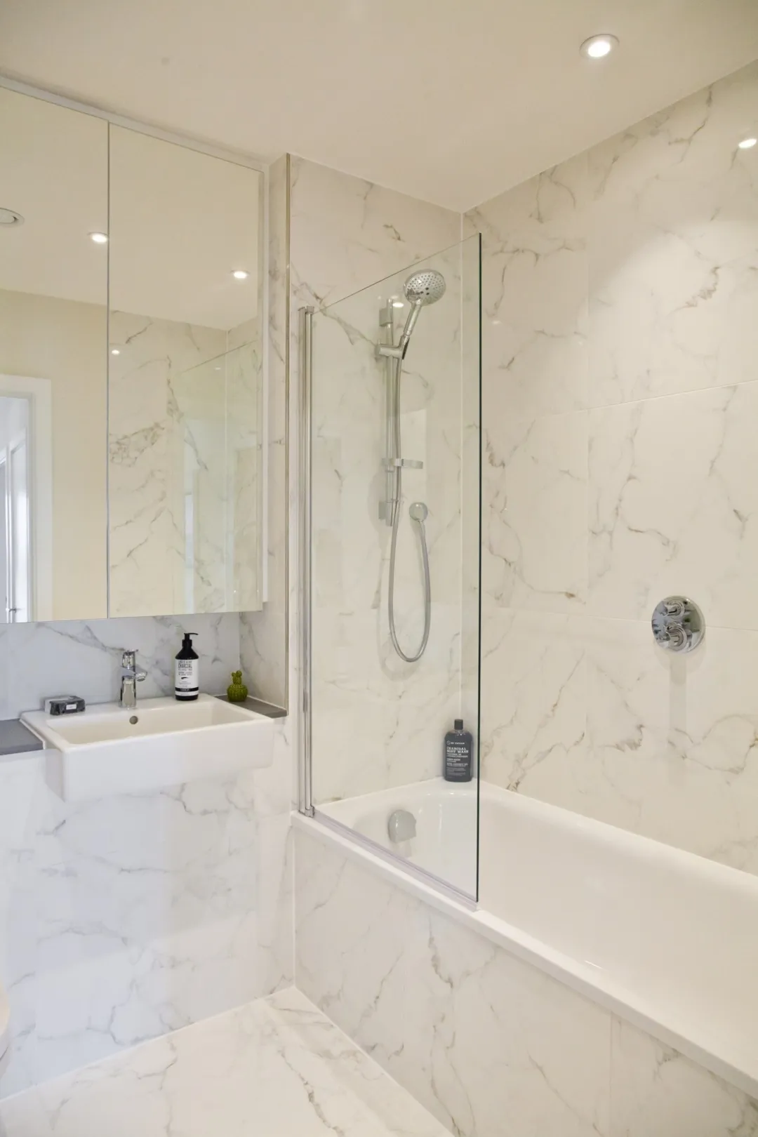 Marble tiled bathroom with large vanity mirror and glass shower screen.