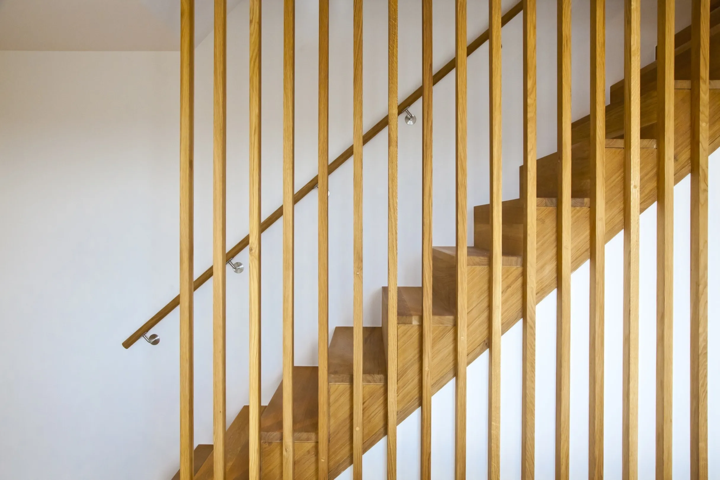 Architectural detail of a modern wooden staircase with floor to ceiling balustrade and a handrail to the wall