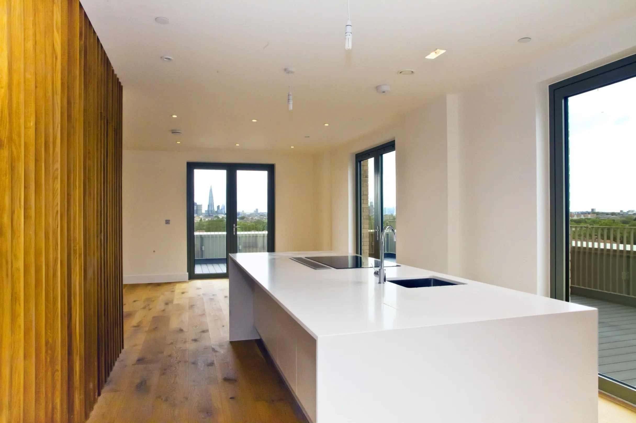 Modern and minimalist kitchen with timber floor, timber feature wall, large kitchen island with built-in appliances and a large wrap-around balcony. The Shard skyscraper is visible in the distance.