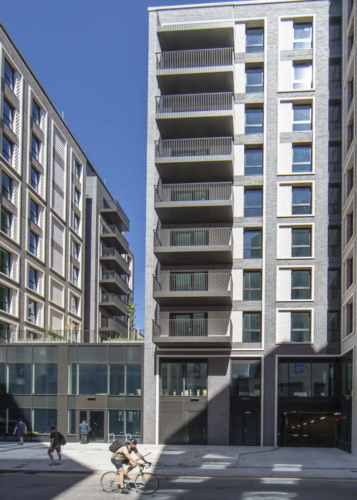 A cyclist passes a modern residential building that is casts a shadow on the road