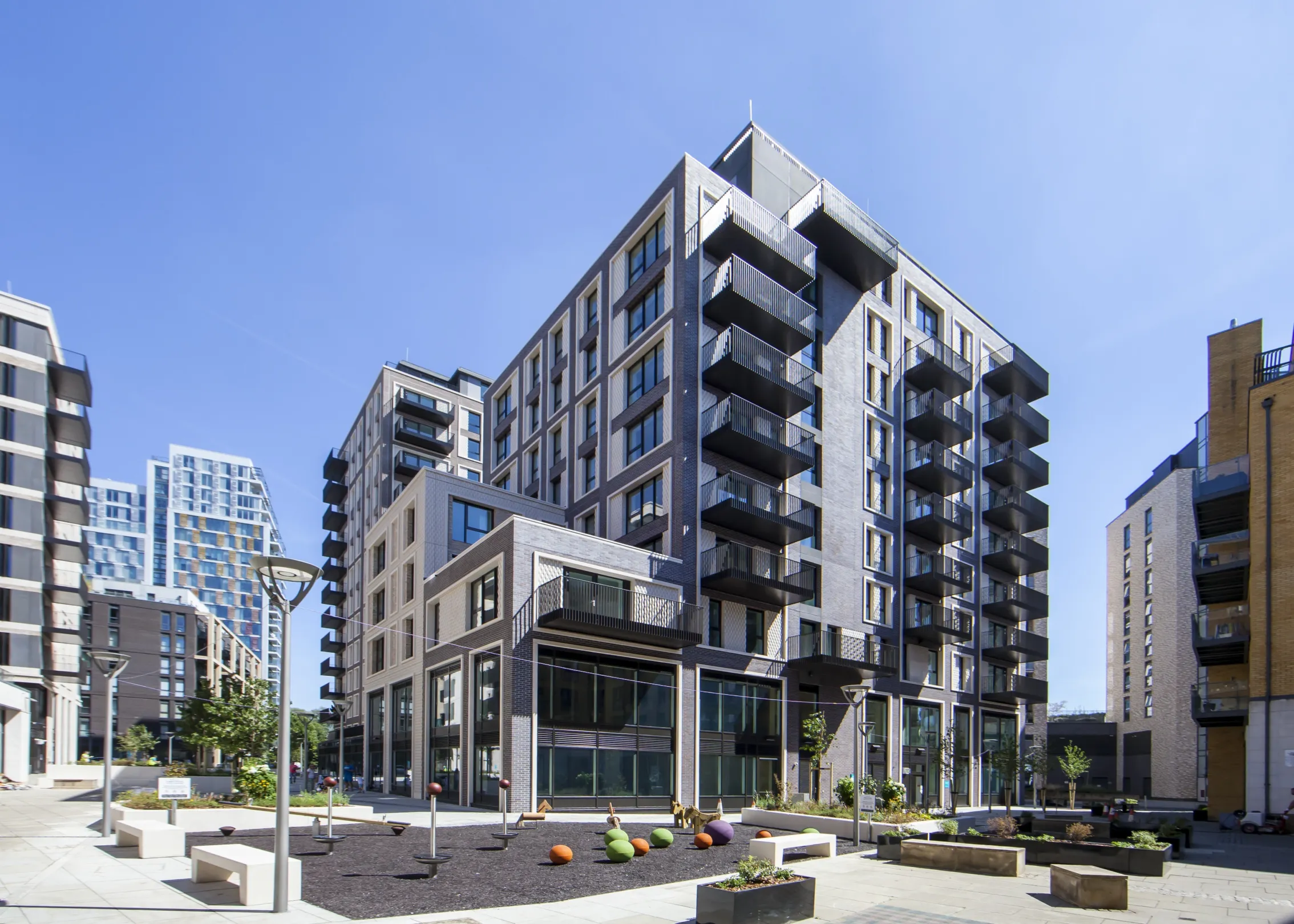 Large modern residential building with balconies, a children's play area in the foreground