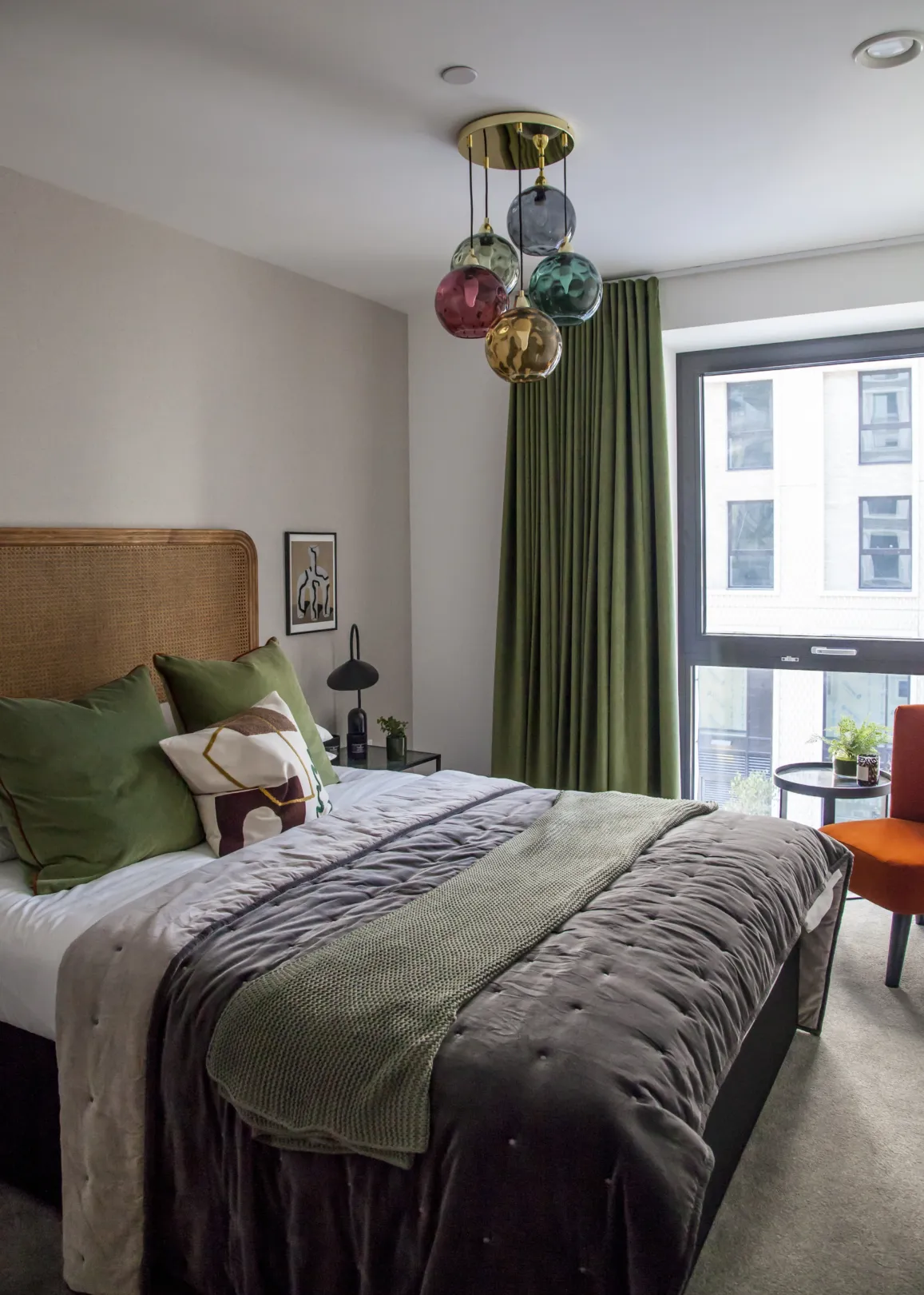 Bedroom interior with layered fabric and plush cushions on the bed, a floor to ceiling curtain and artistic class pendant light