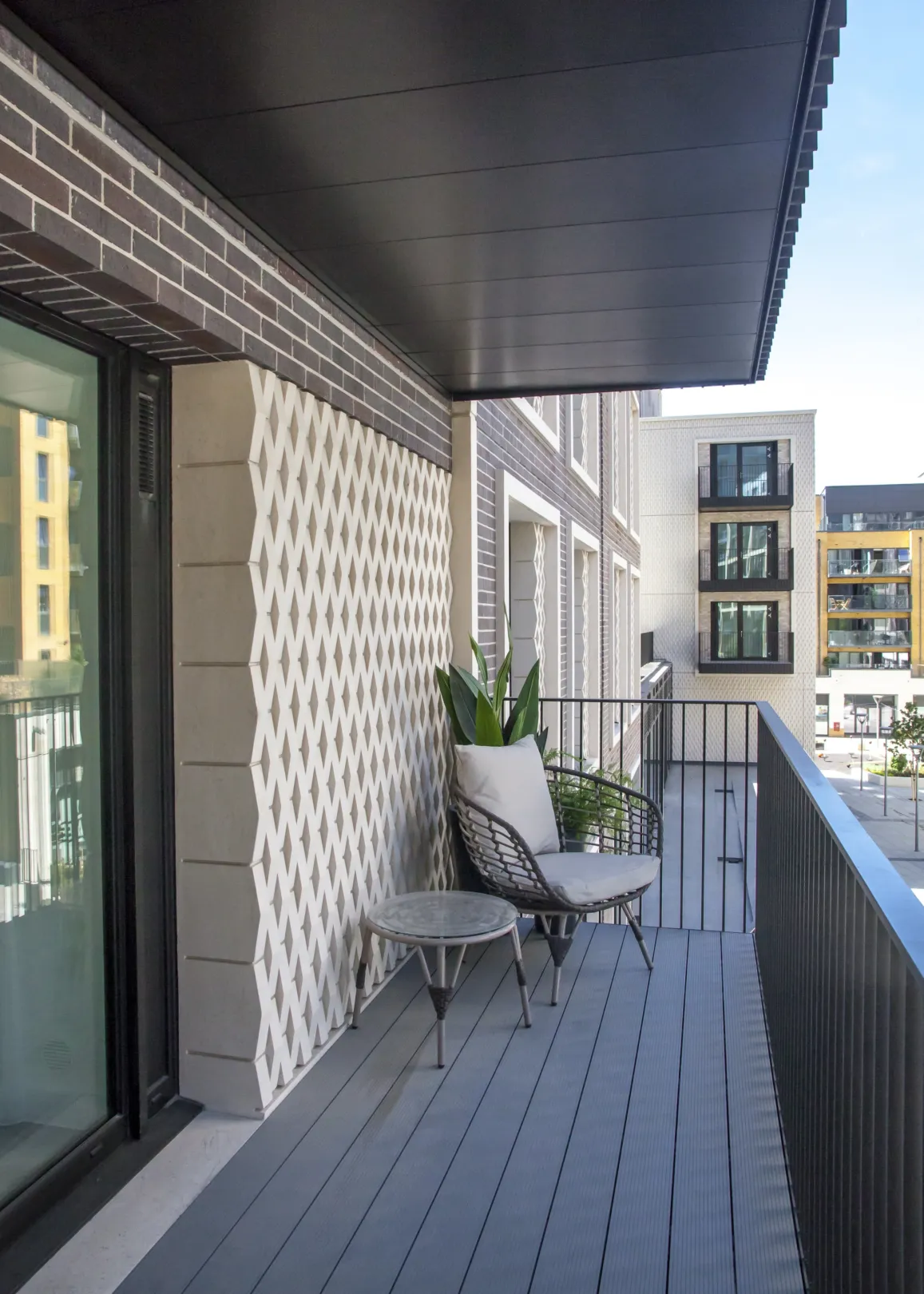 A chair and side table on a private balcony with textured tiling detail to the exterior wall