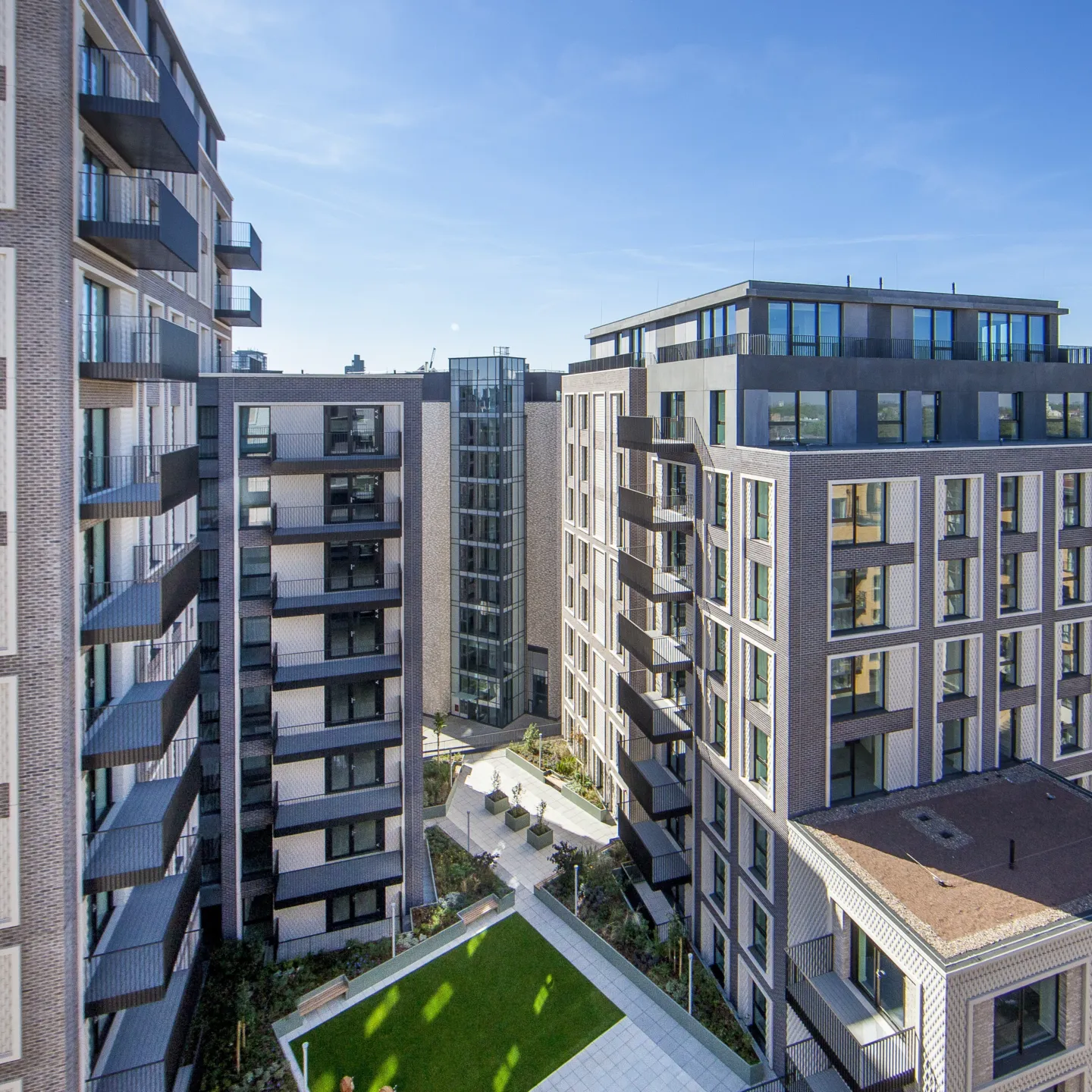 A large residential development from a high vantage point, showing a raise lawned area, balconies, and reflections cast from windows.