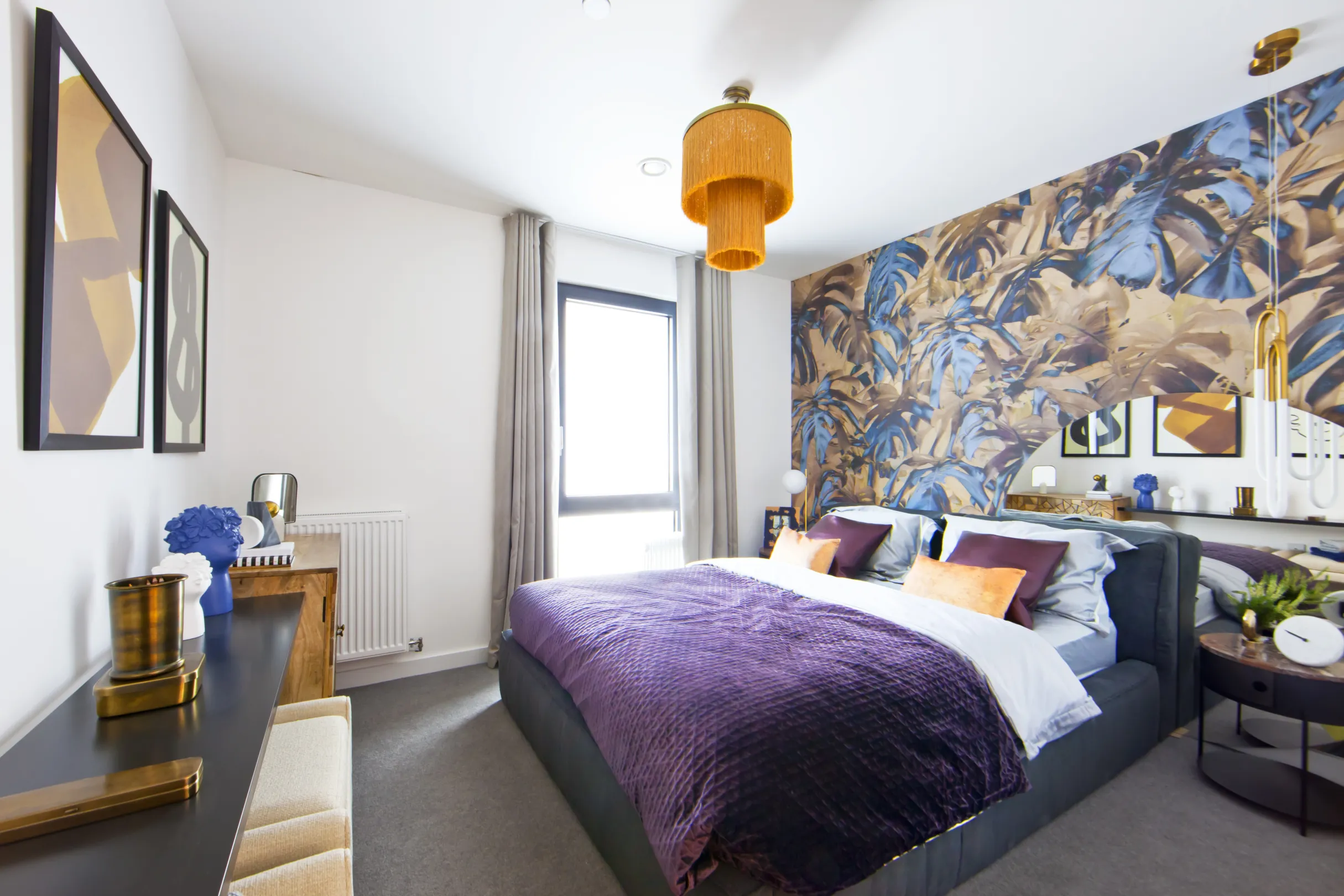 A vibrant double bedroom with blue and gold feature wallpaper behind the bed.