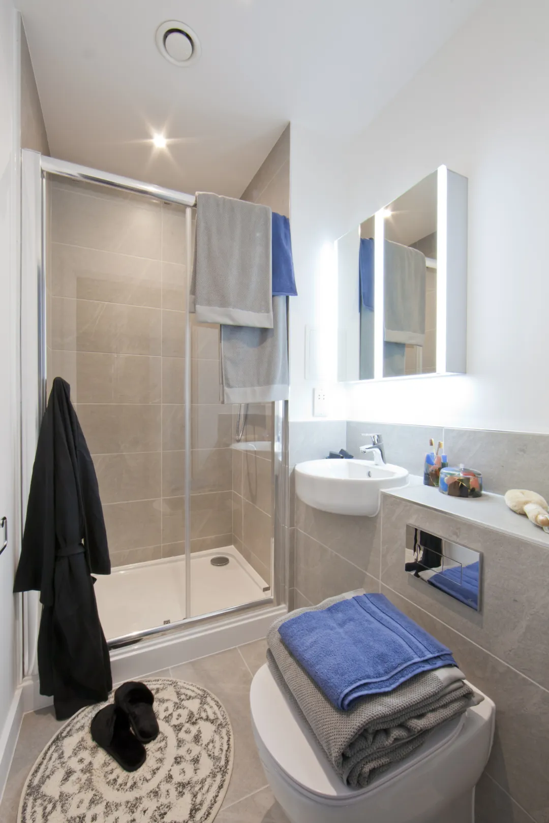A fully tiled bathroom with chrome ironmongery, a mirrored cabinet on the wall and a semi recessed basin