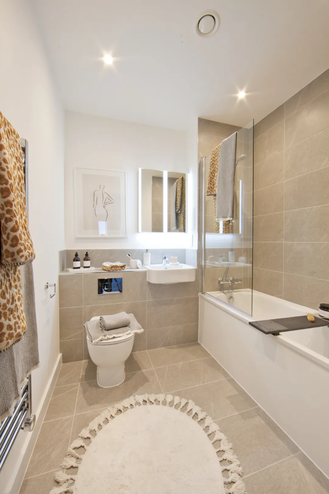 A fully tiled bathroom with chrome ironmongery, a mirrored cabinet on the wall and a semi recessed basin