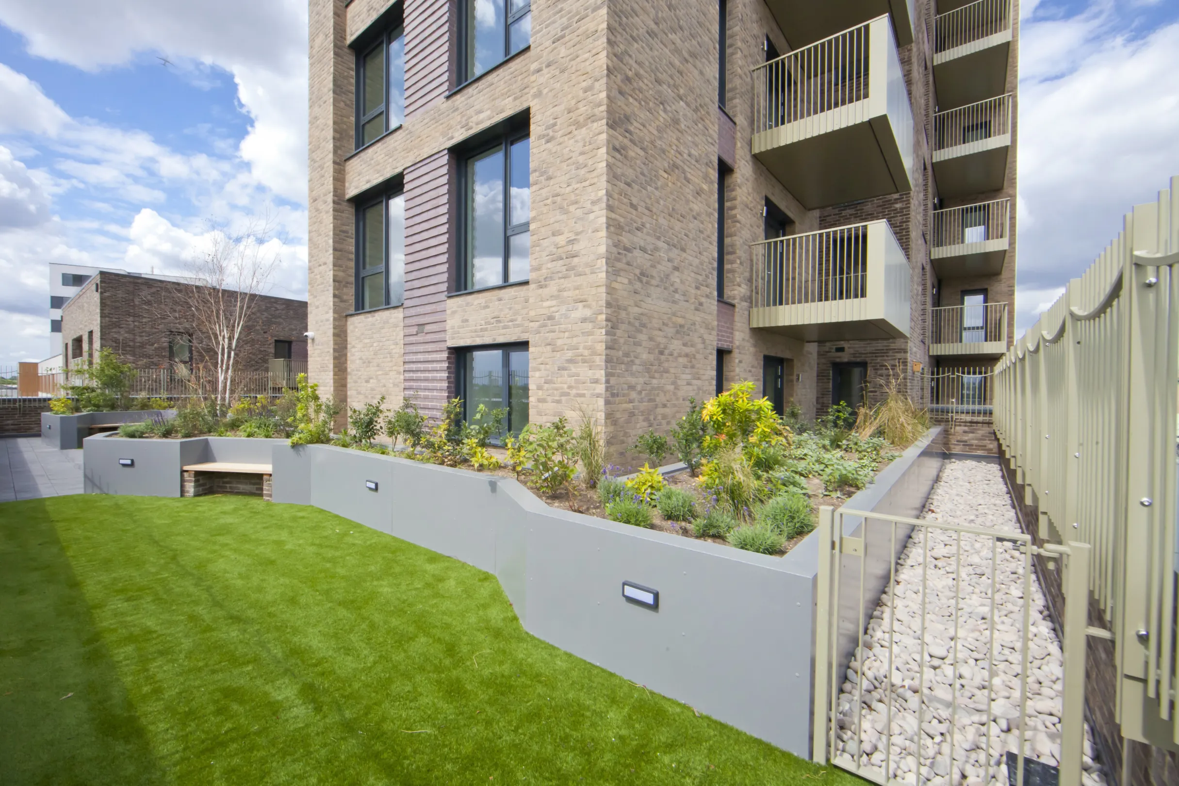 A modern brick facade residential building with lawned  grounds and a gravel pathway behind a gate