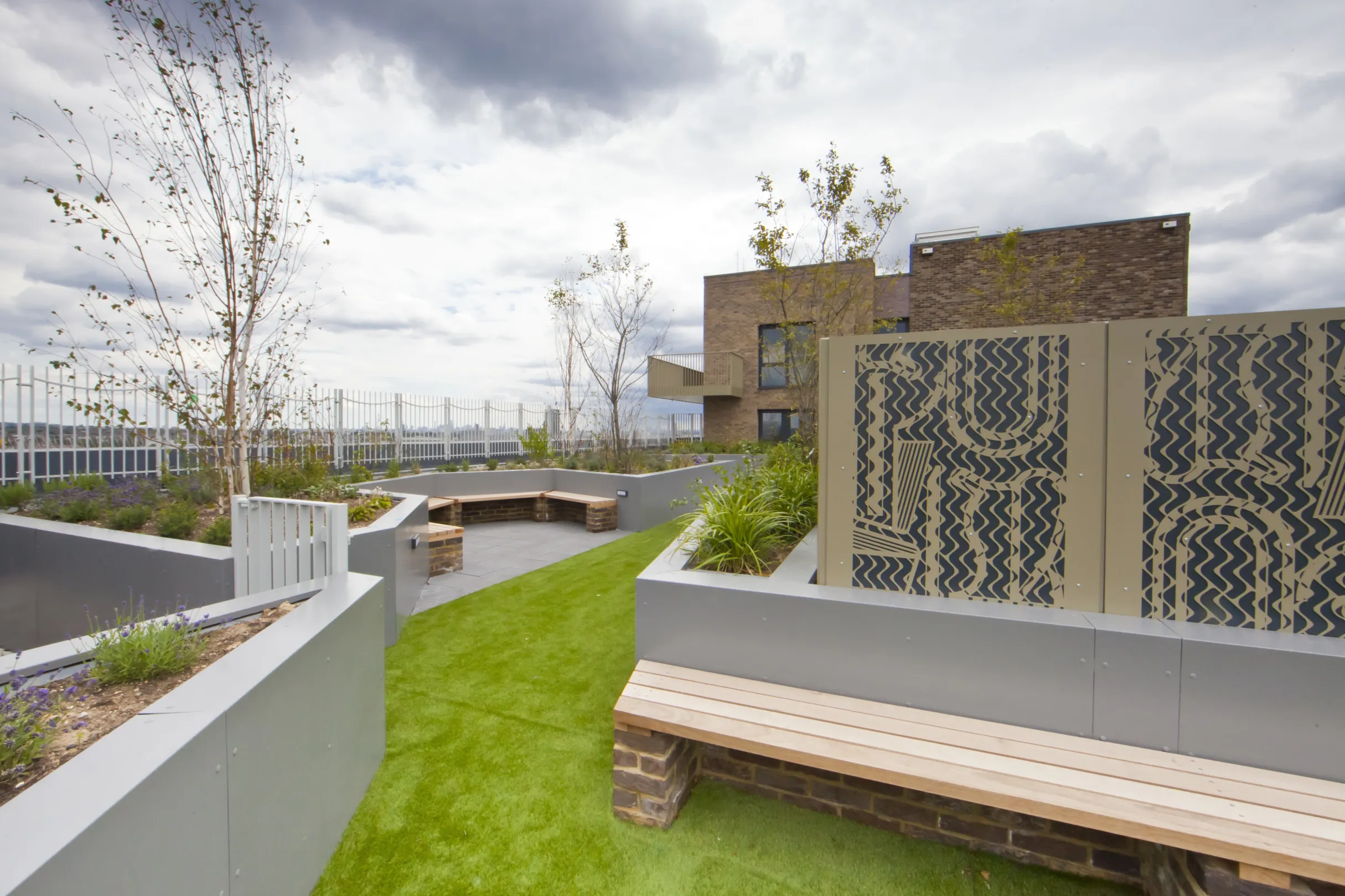 A modern rooftop garden with wooden bench seating and feature panel