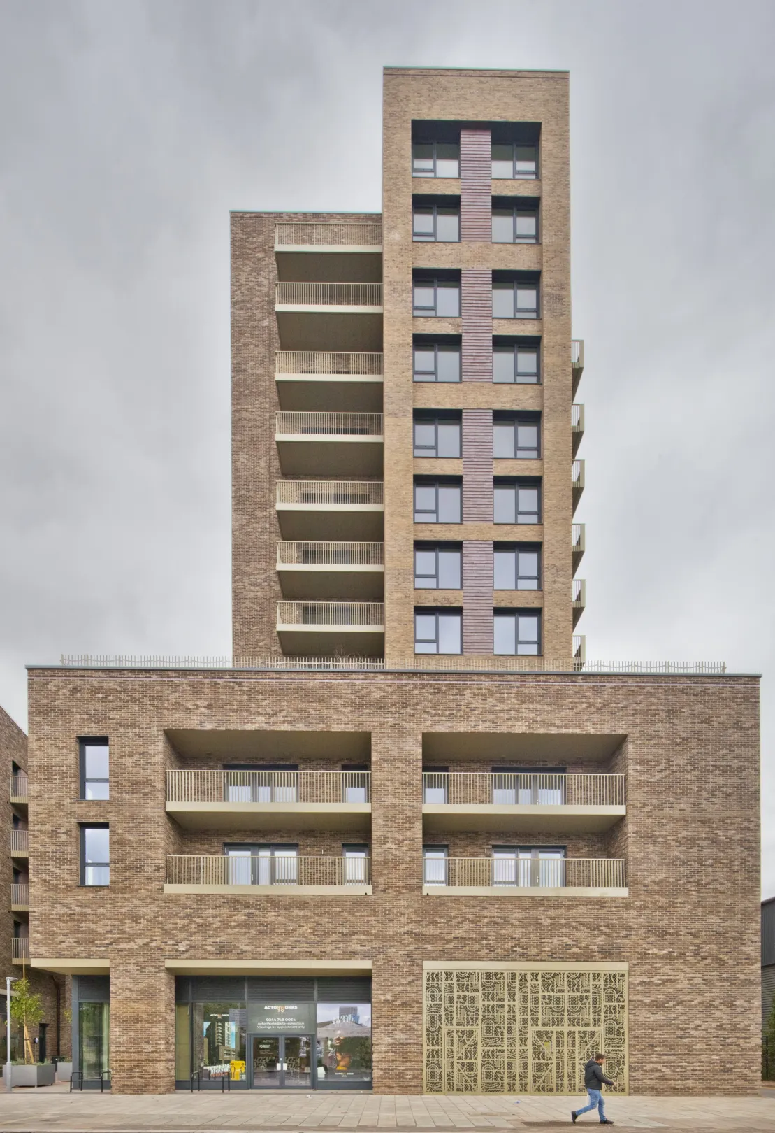 A modern multi storey residential building with balconies on the facade and trees and ornate, patterned metalwork at the foyer