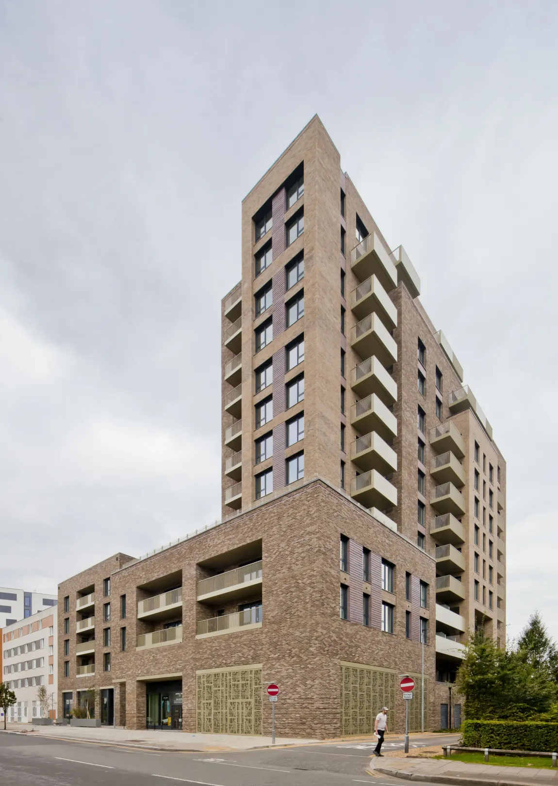 A modern multi storey residential building with balconies on the facade and trees and ornate, patterned metalwork at the foyer