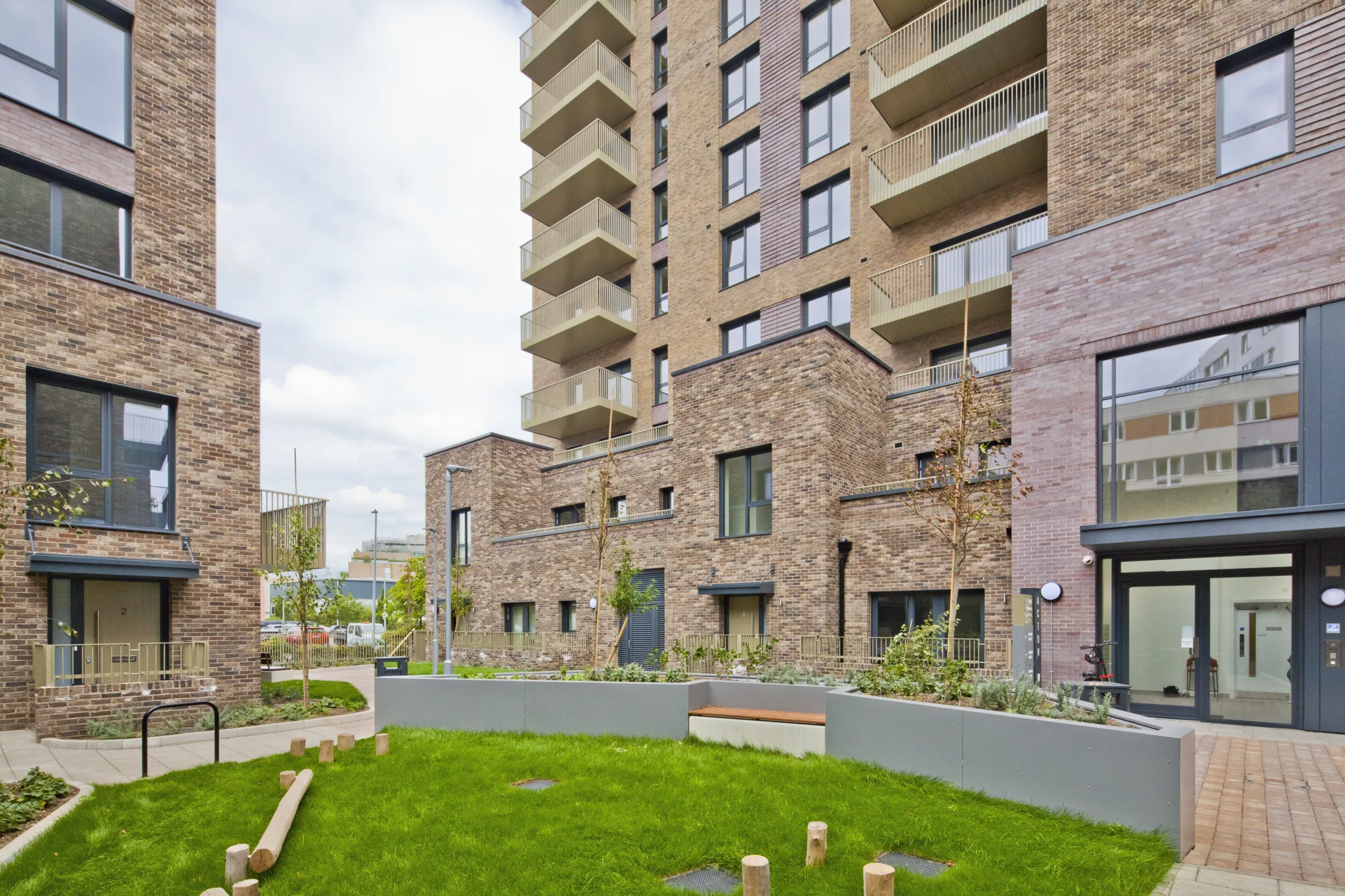 A modern multi storey residential building with balconies on the facade and a small lawn with children's play area