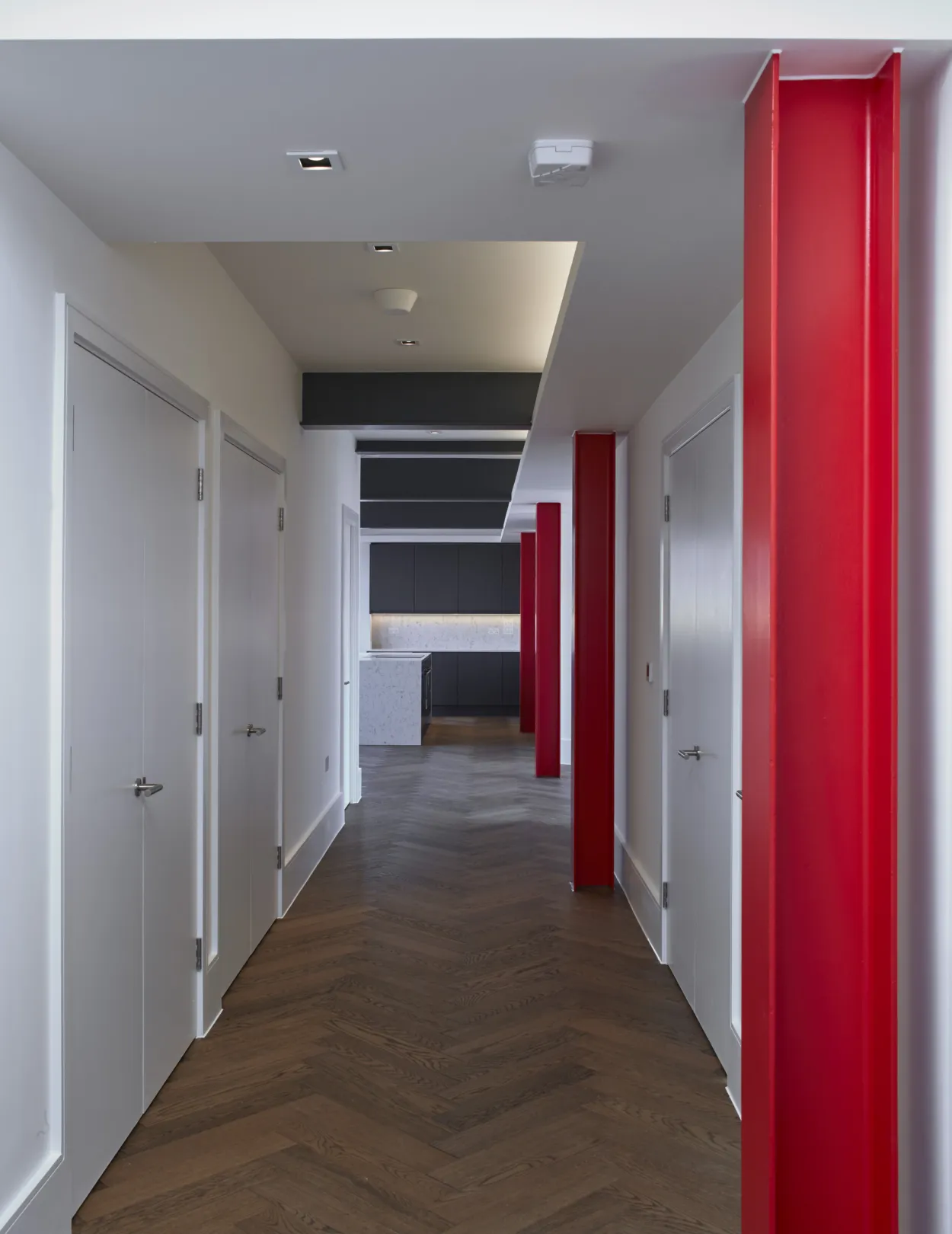 Modern large aparment, with grey kitchen, marble white worktop, integrated appliances, herrinbone flooring and red steelwork