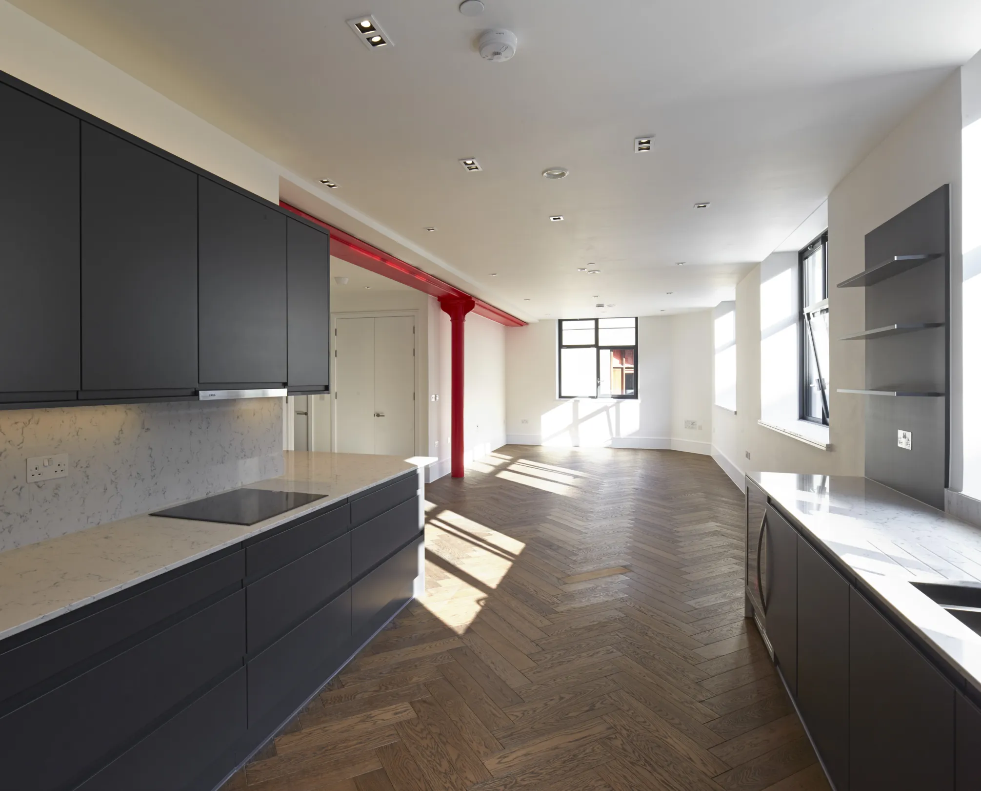 Modern large aparment, with grey kitchen, marble white worktop, integrated appliances, herrinbone flooring and red steelwork