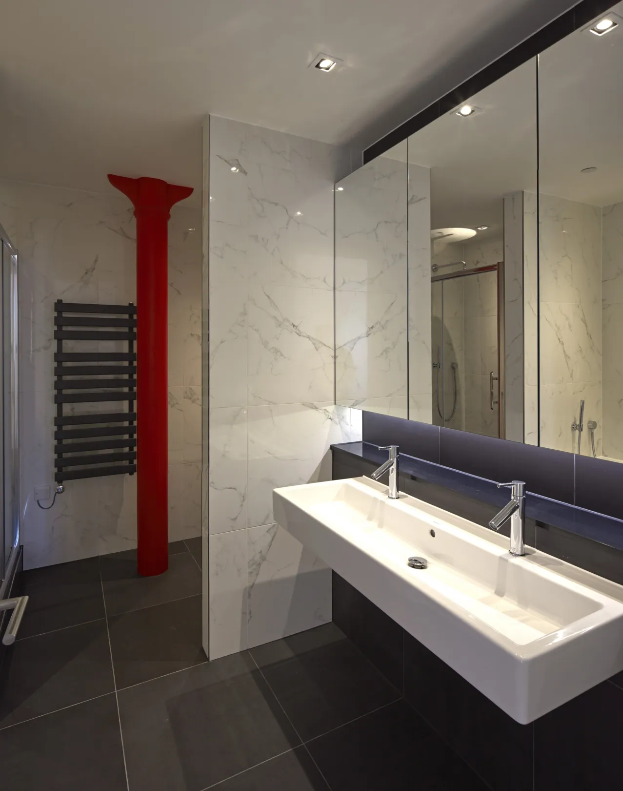 Modern bathroom with large double white sink and tiled floor and walls.  Large mirrored cabinet above basin.