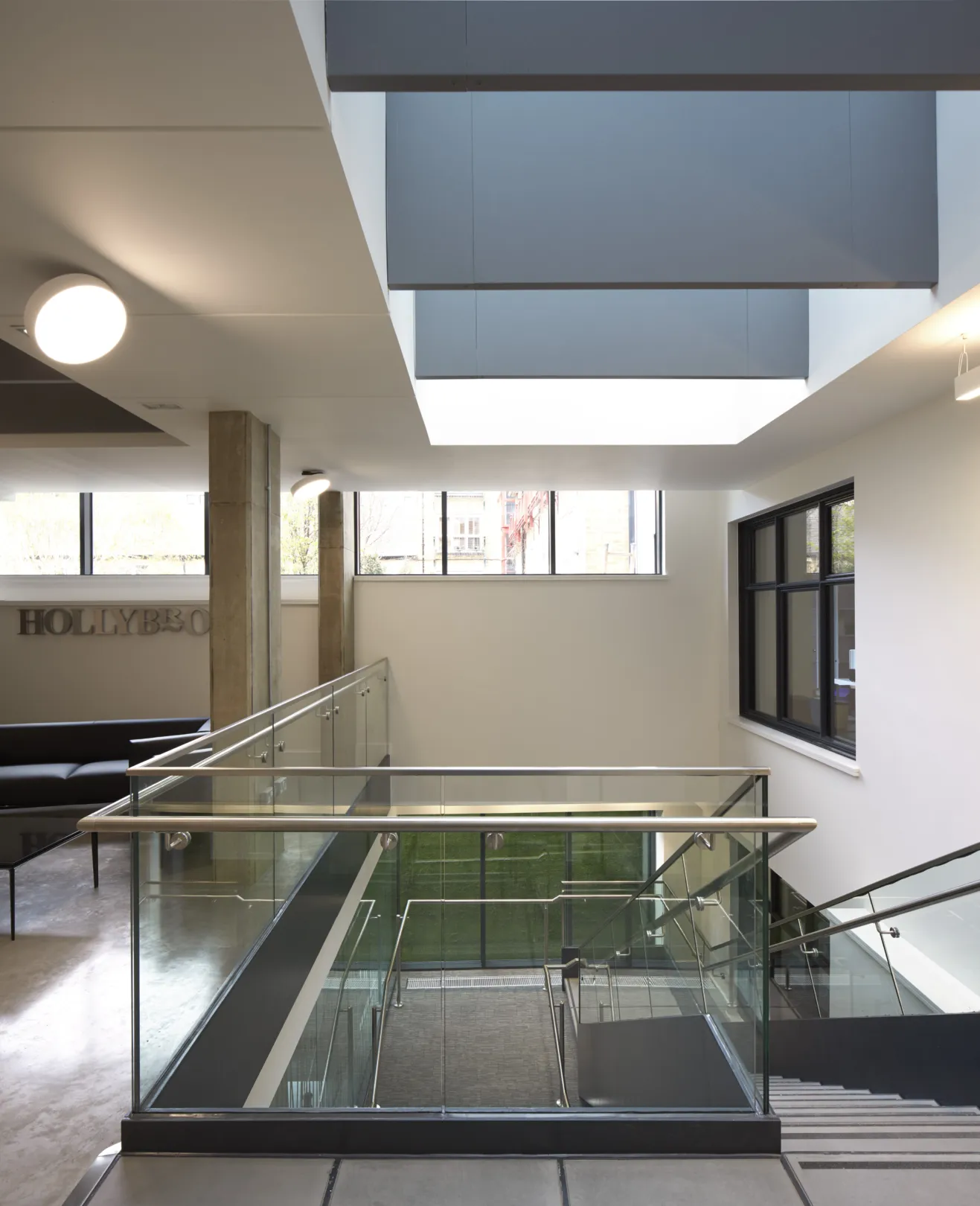 Modern office interior at lower ground level showing glass offices and central staircase in modern ironwork.