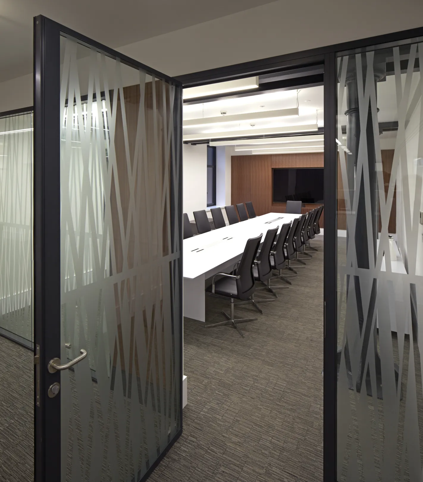 Modern office interior at lower ground level showing glass offices and central staircase in modern ironwork.