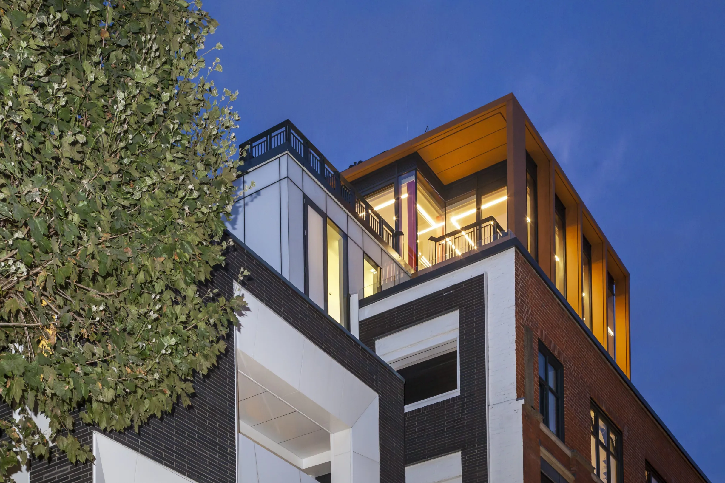 Top floors of a modern residential illuminated at night, showing large windows and balconies at penthouse level.