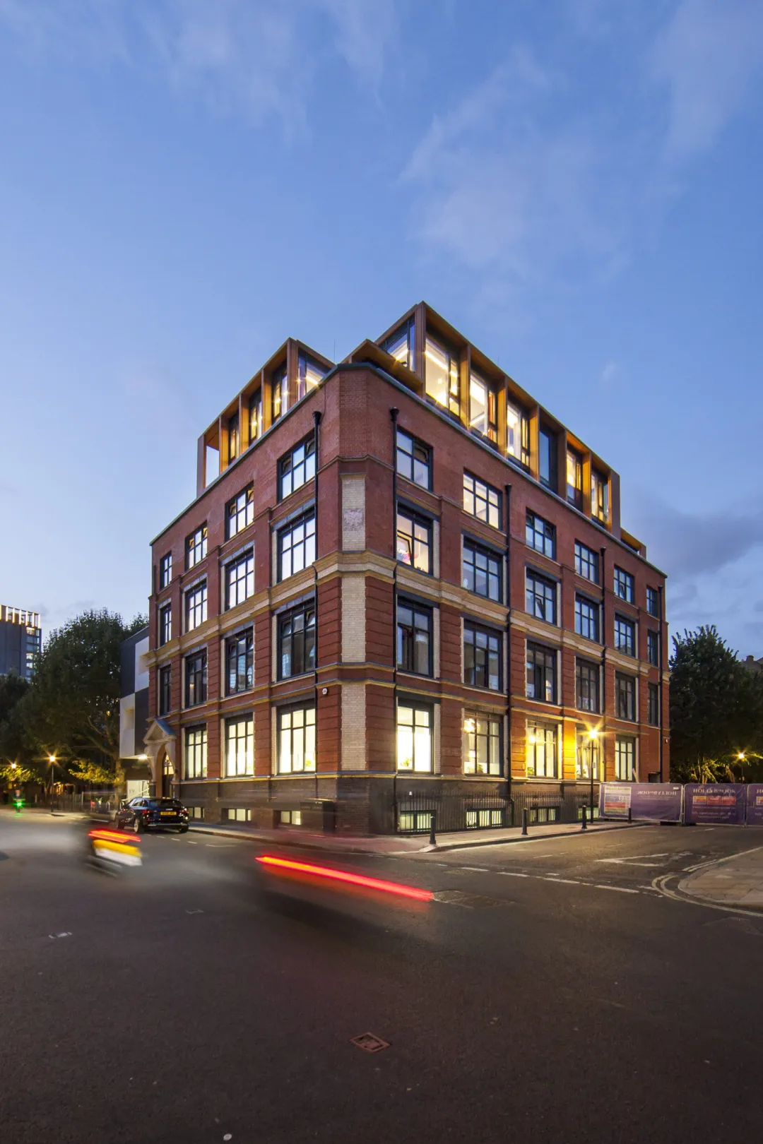 A 6 storey residential building entrance illuminated at night, with red car streaking across the foreground