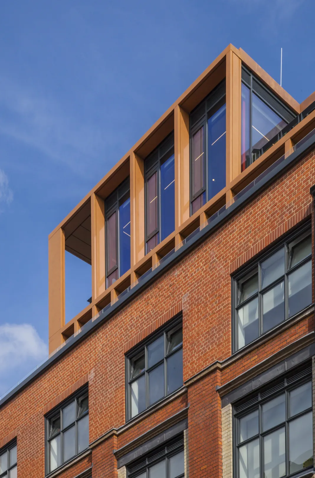 Top floors of a modern residential building in red brick, showing large windows and balconies at penthouse level.