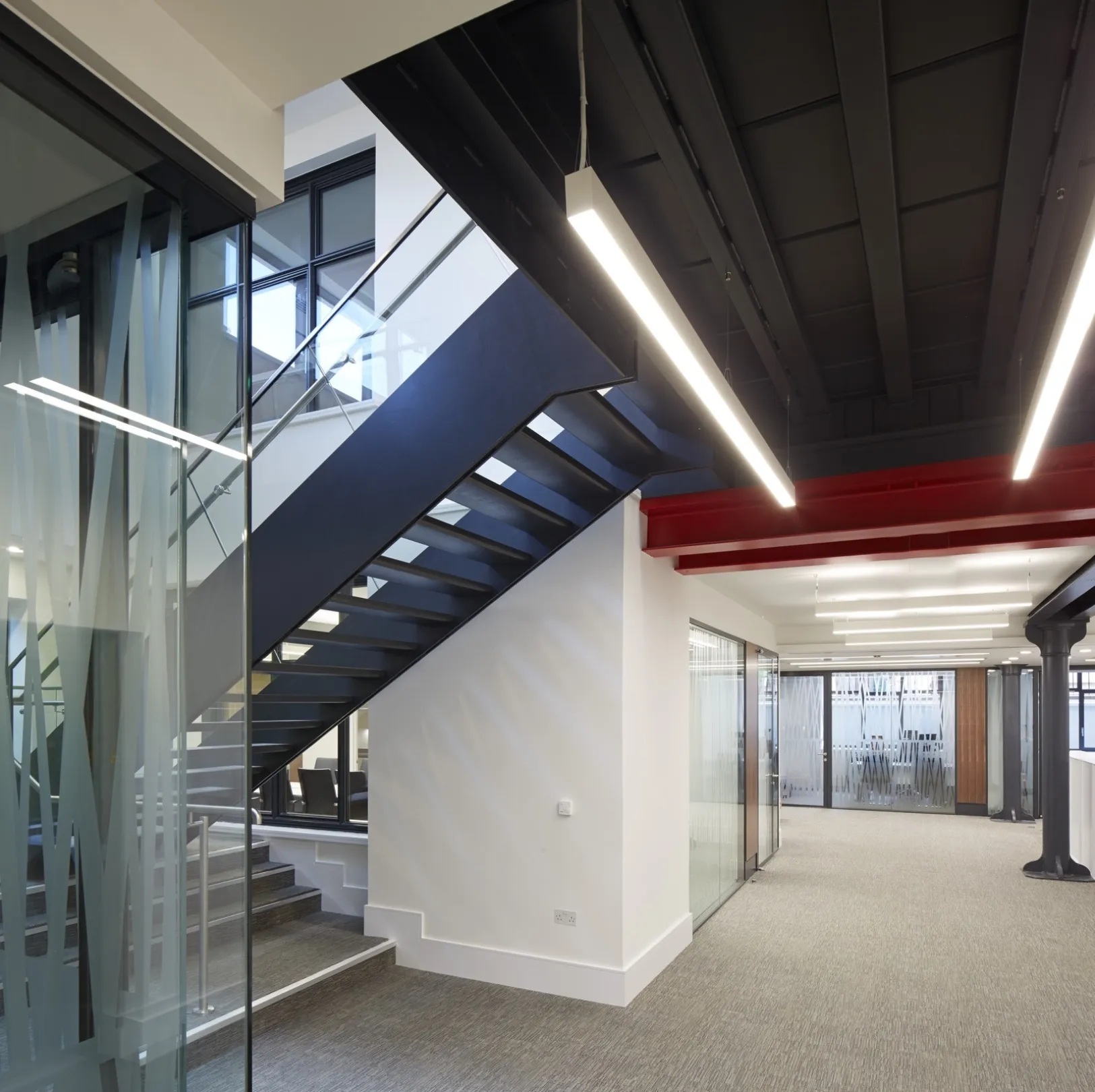 Modern office interior at lower ground level showing glass offices and central staircase in modern ironwork.