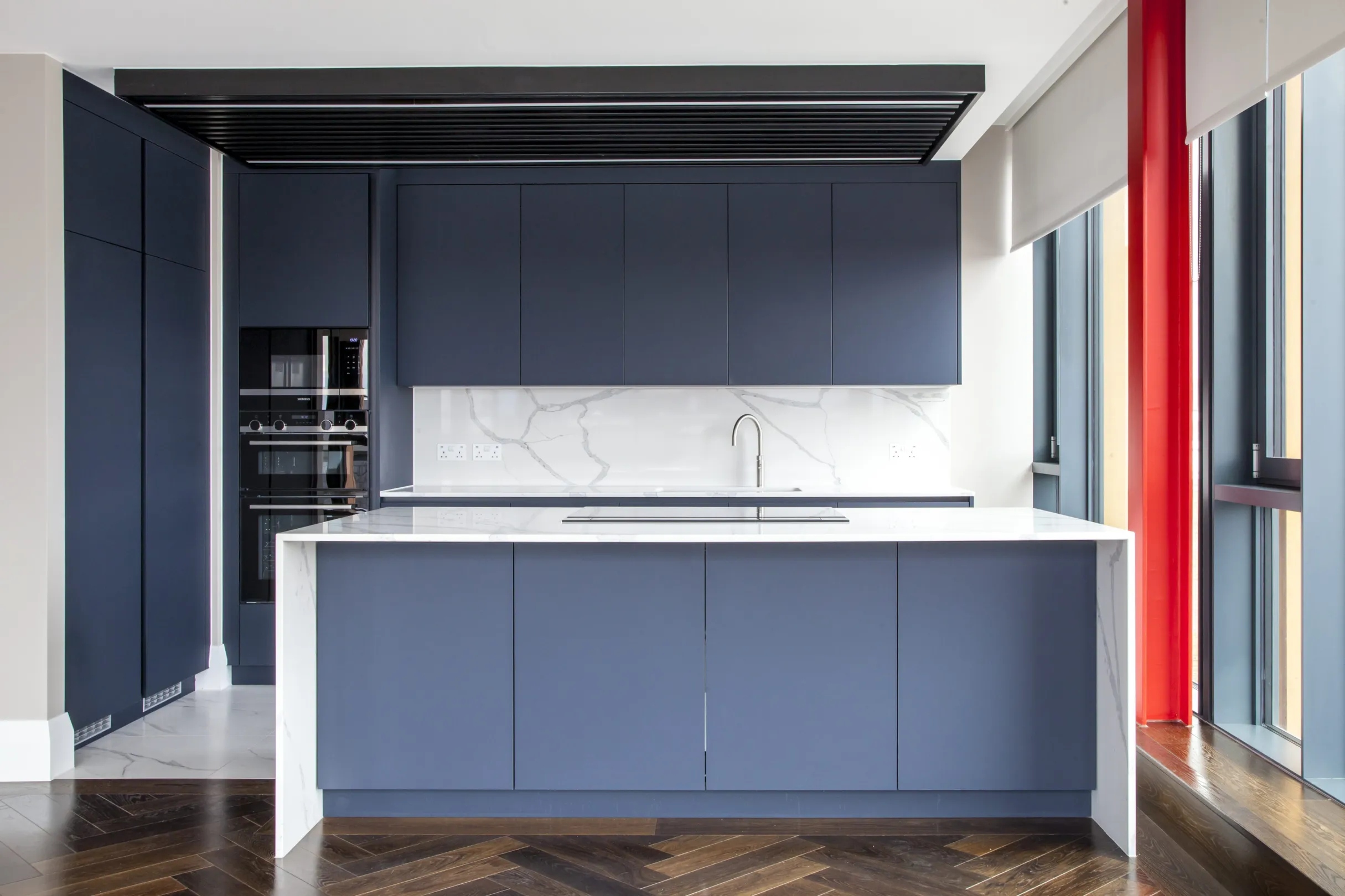 Modern designed kitchen with island and breakfast bar, dark blue/grey cabinets and marble back splash.