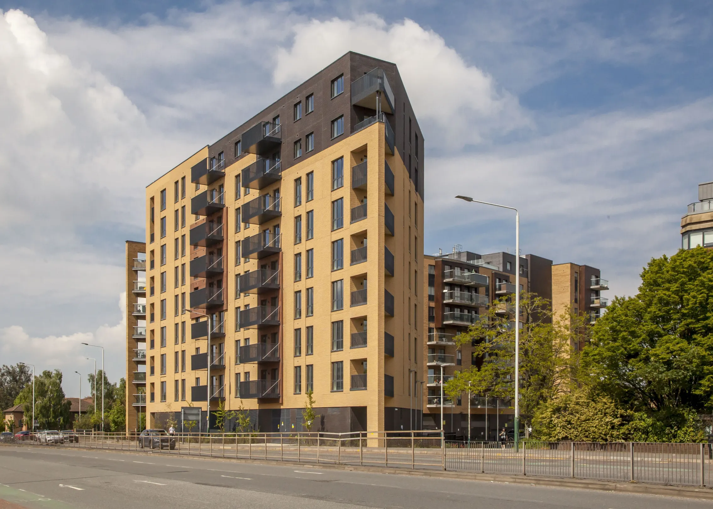 View from the road of a 9 storey residential building adjacent to mature trees in full leaf