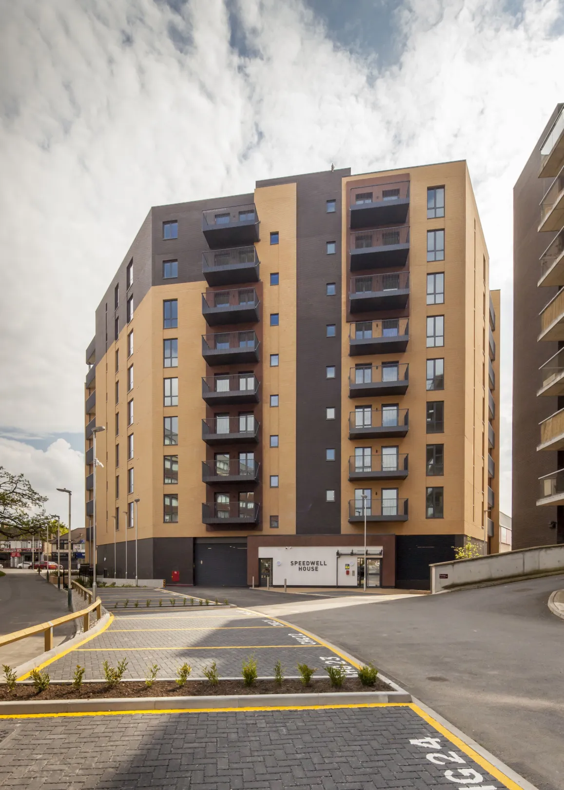 Exterior view of a 9 storey residential building with balconies and car parking spaces in the foreground
