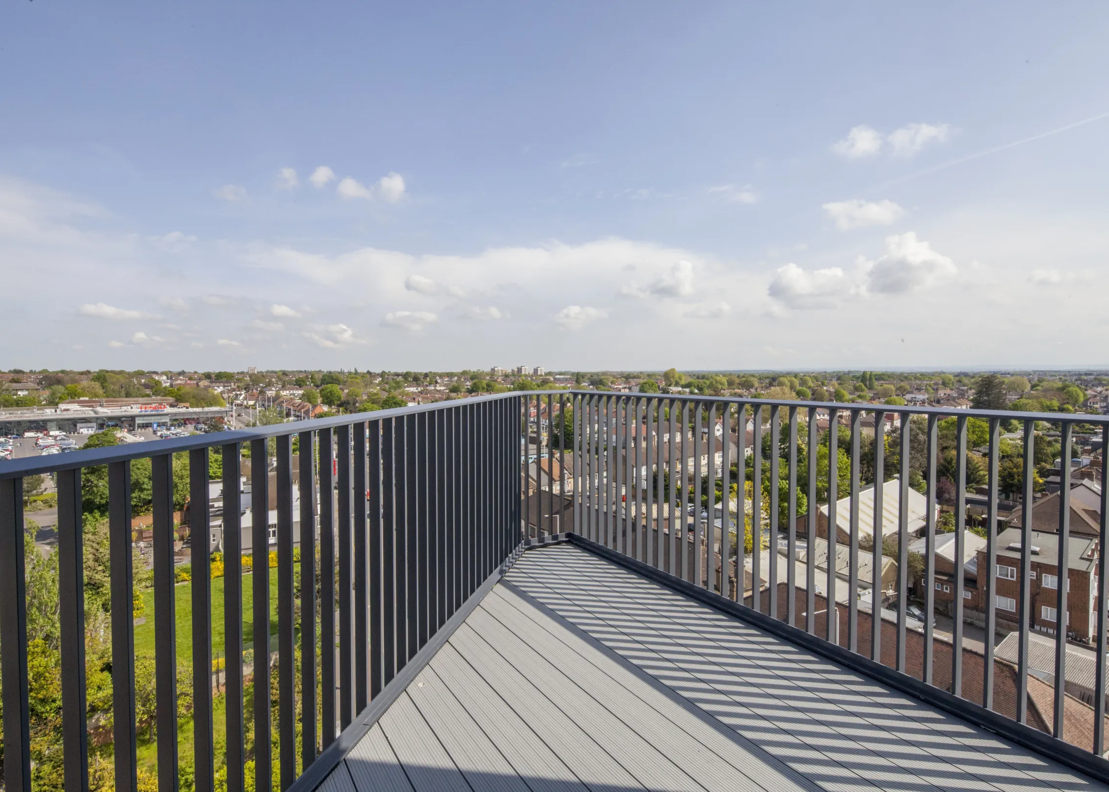 View from a modern residential balcony across a leafy suburban landscape to the horizon