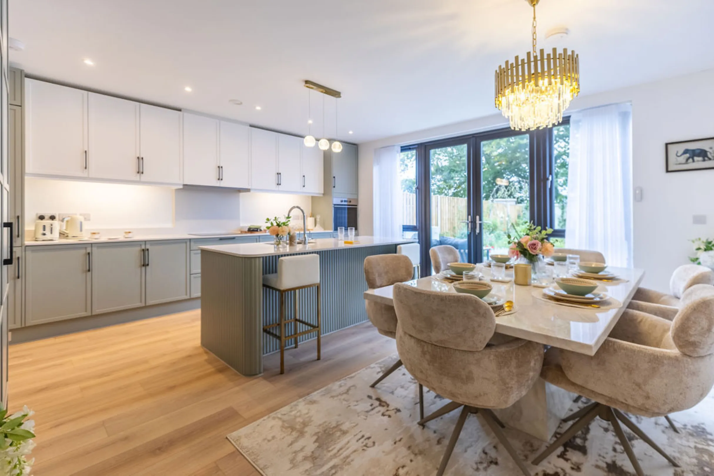 The image showcases a modern kitchen and dining area. It features a kitchen with white and teal cabinetry, a kitchen island with bar stools, and a dining table set for a meal.