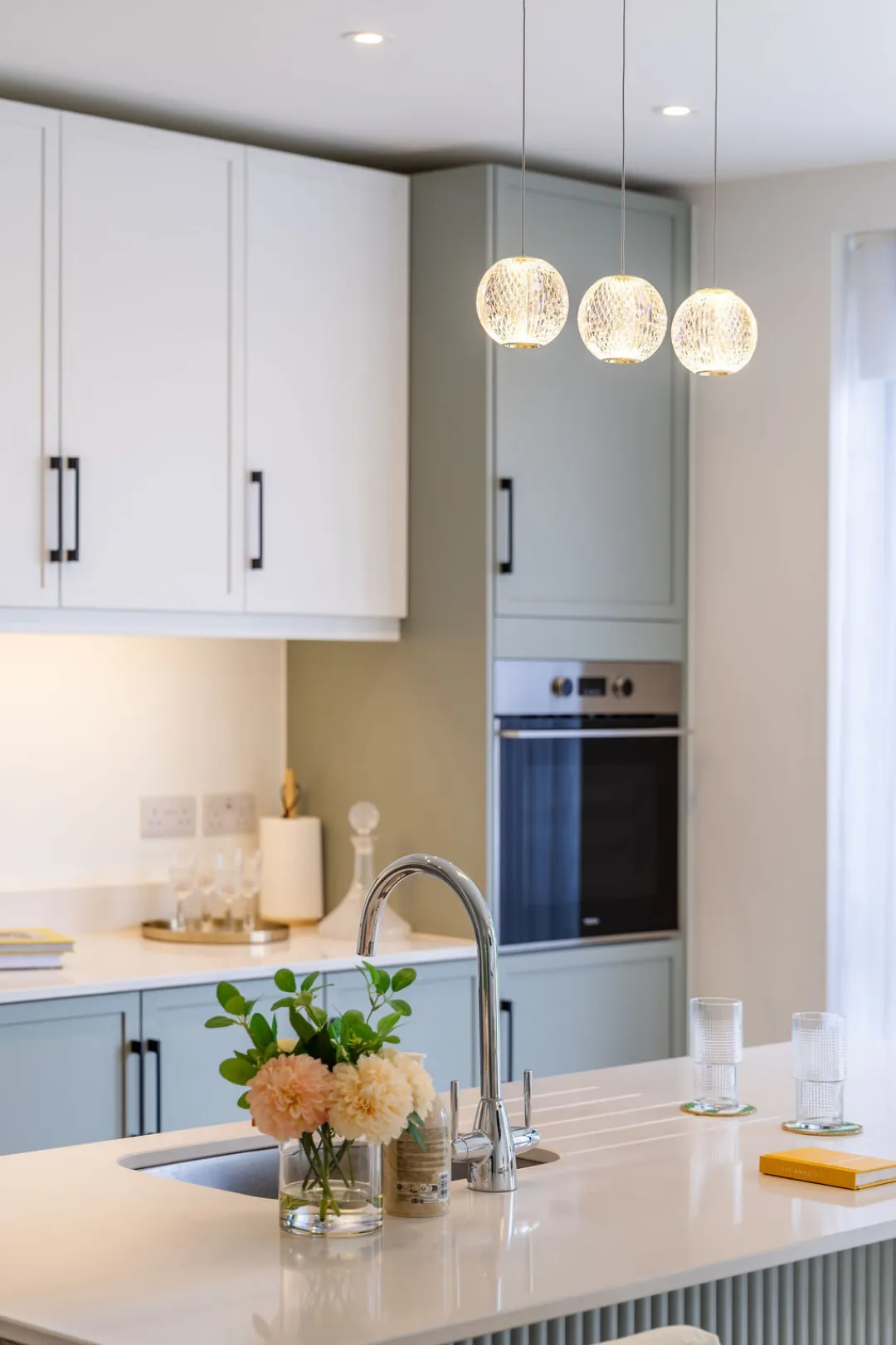 The image showcases a modern kitchen with white and teal cabinetry, a kitchen island with bar stools