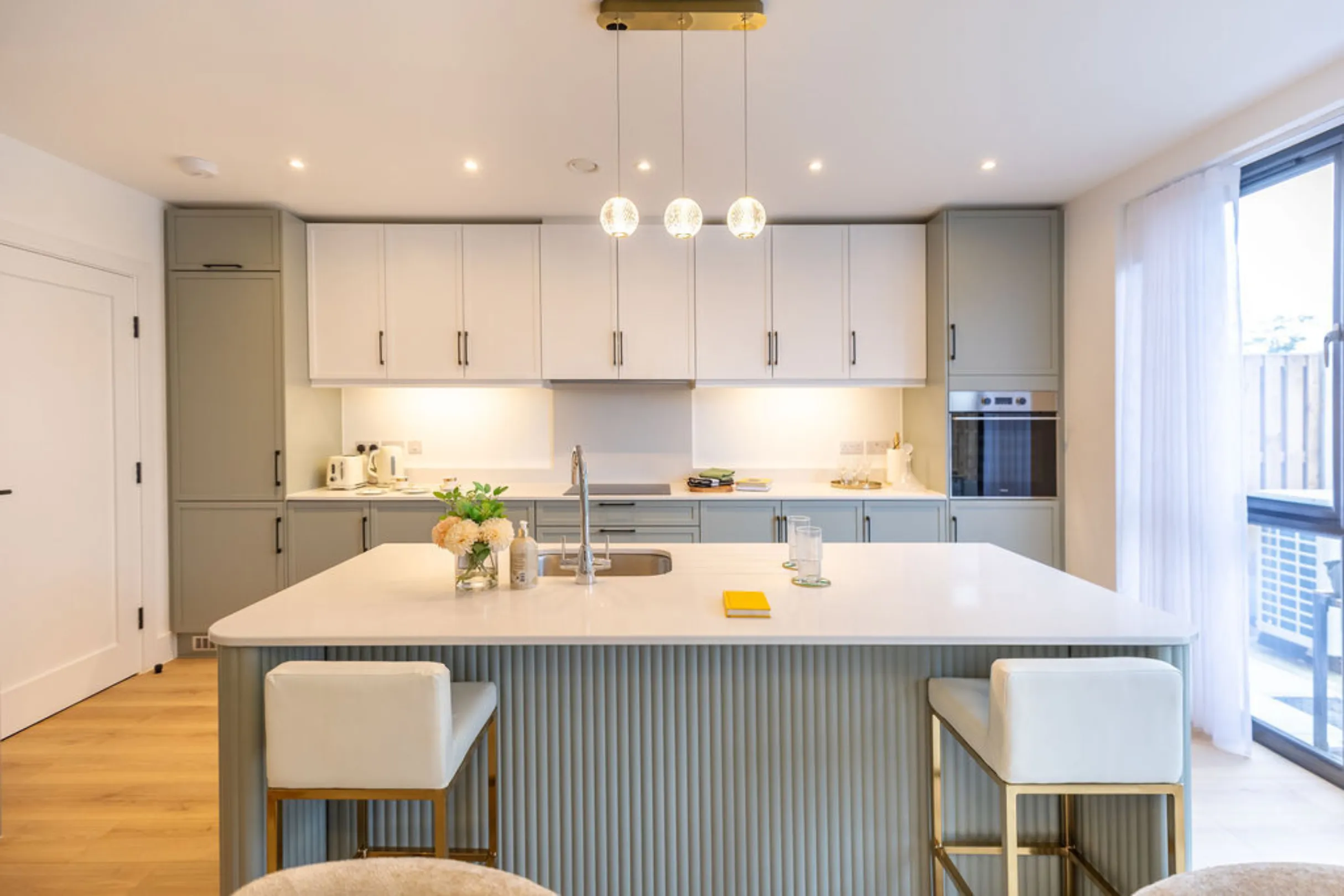 The image showcases a modern kitchen with white and teal cabinetry, a kitchen island with bar stools