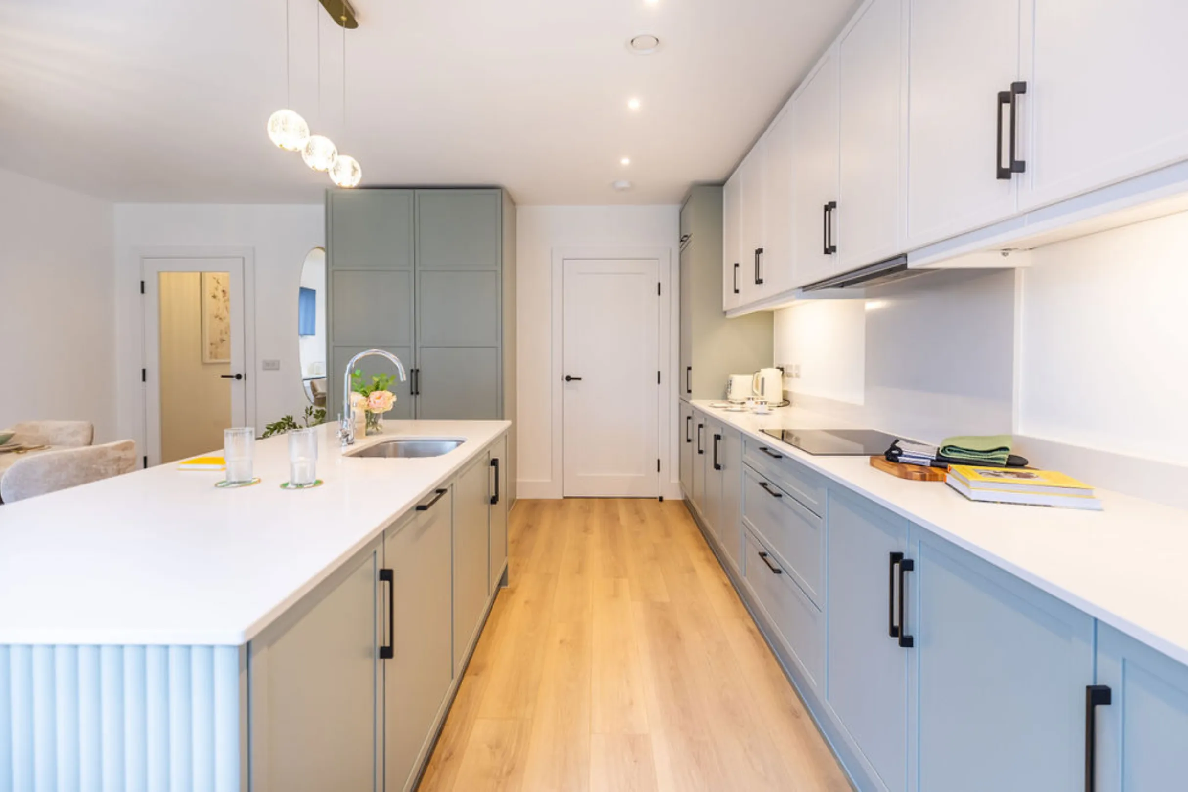 The image showcases a modern kitchen with white and teal cabinetry, a kitchen island with bar stools