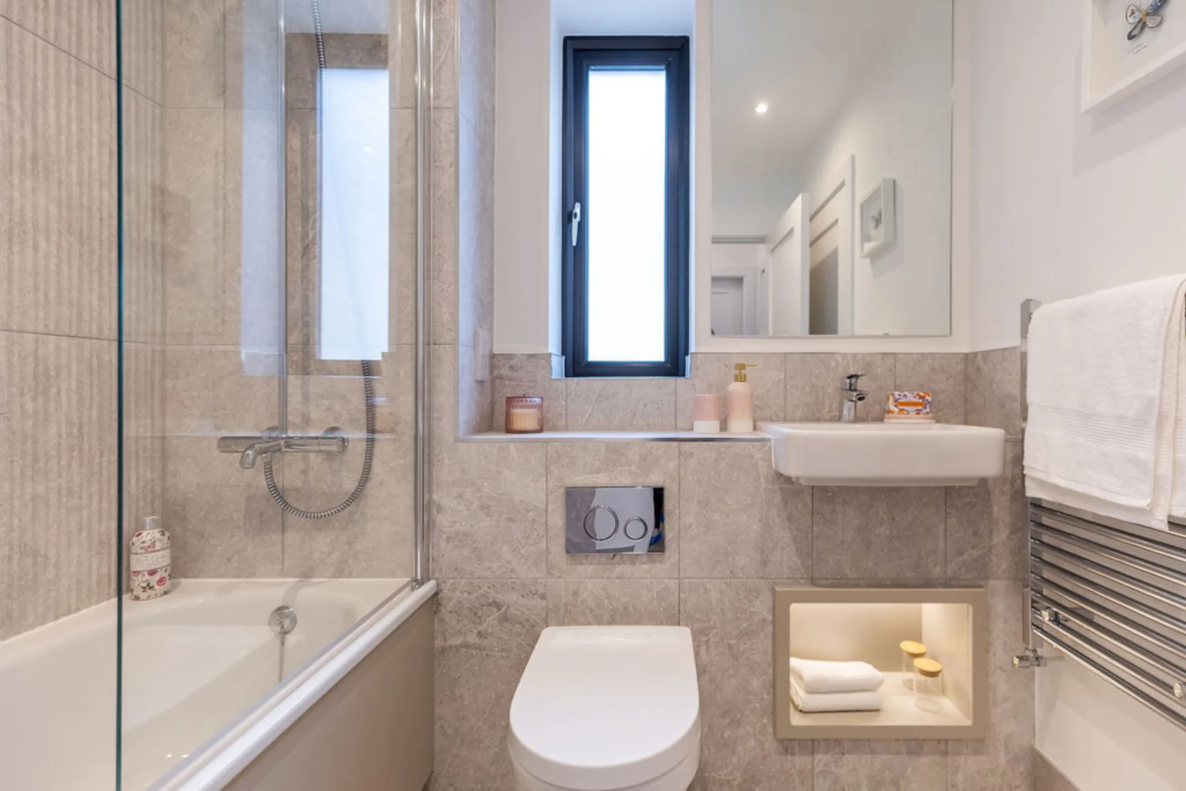 The image shows a modern bathroom with a toilet, sink, and decorative elements. The bathroom has gray tiles, a white toilet, and framed artwork.