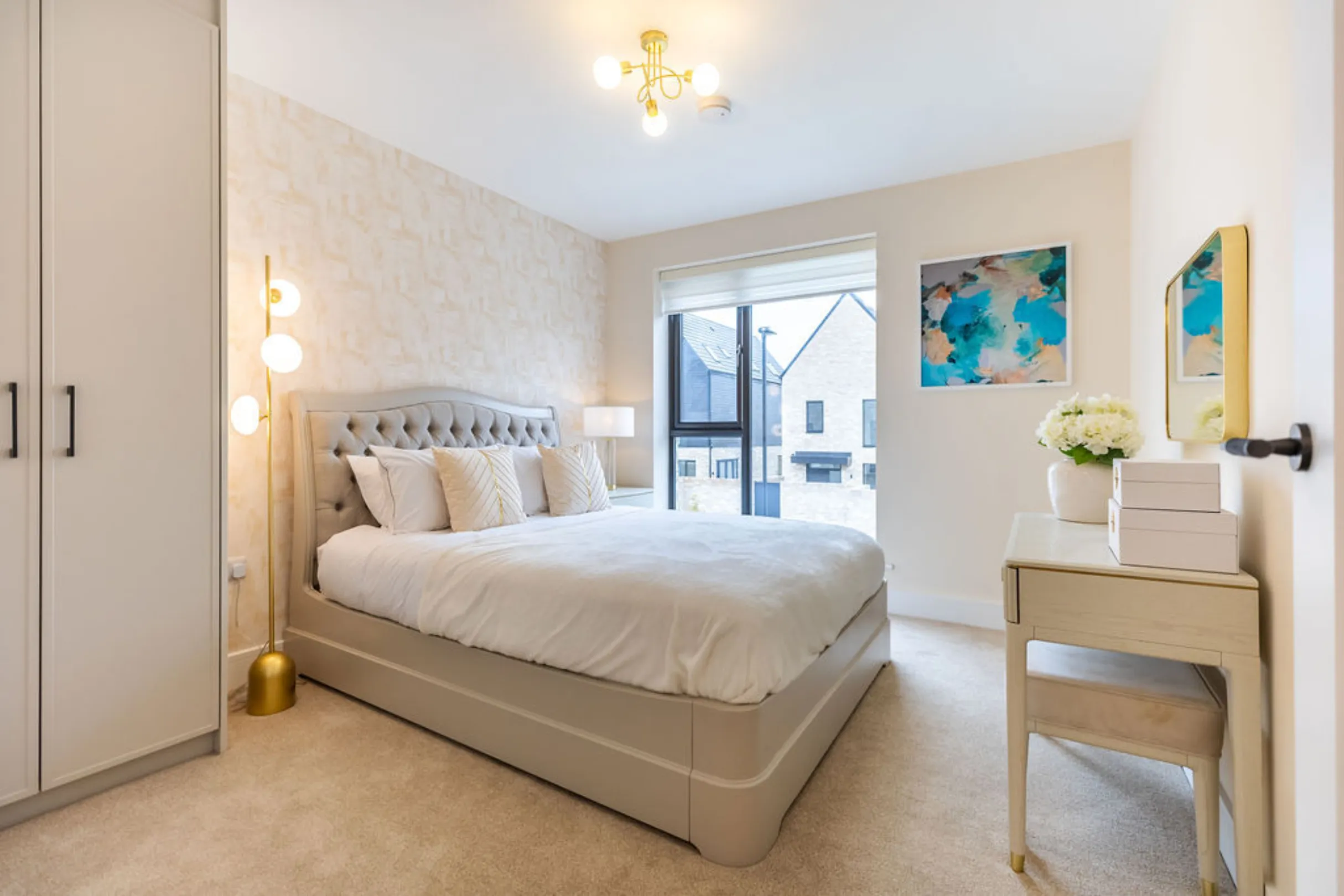 The image showcases a well-lit bedroom with a bed, a wardrobe, and a small dressing table. The room is decorated with soft colors and modern furniture.