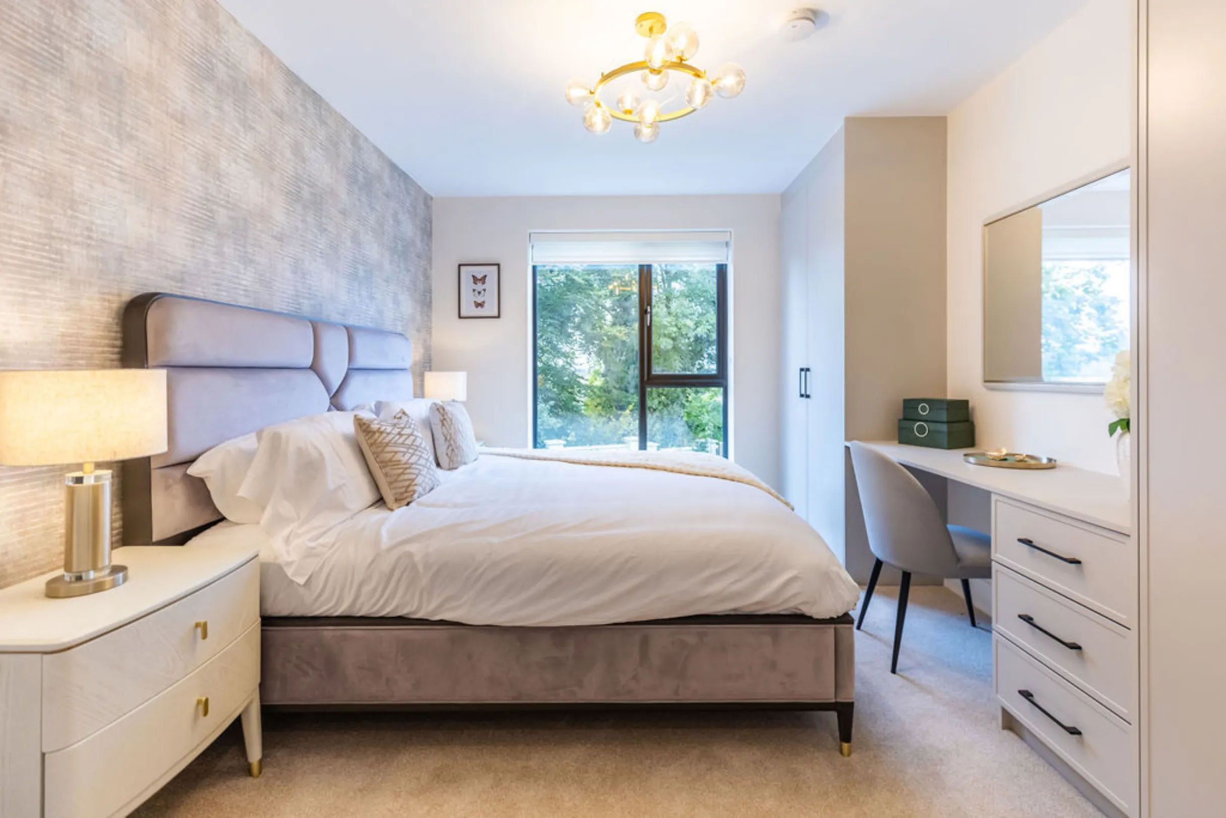 The image showcases a well-lit bedroom with a bed, a wardrobe, and a small dressing table. The room is decorated with soft colors and modern furniture.