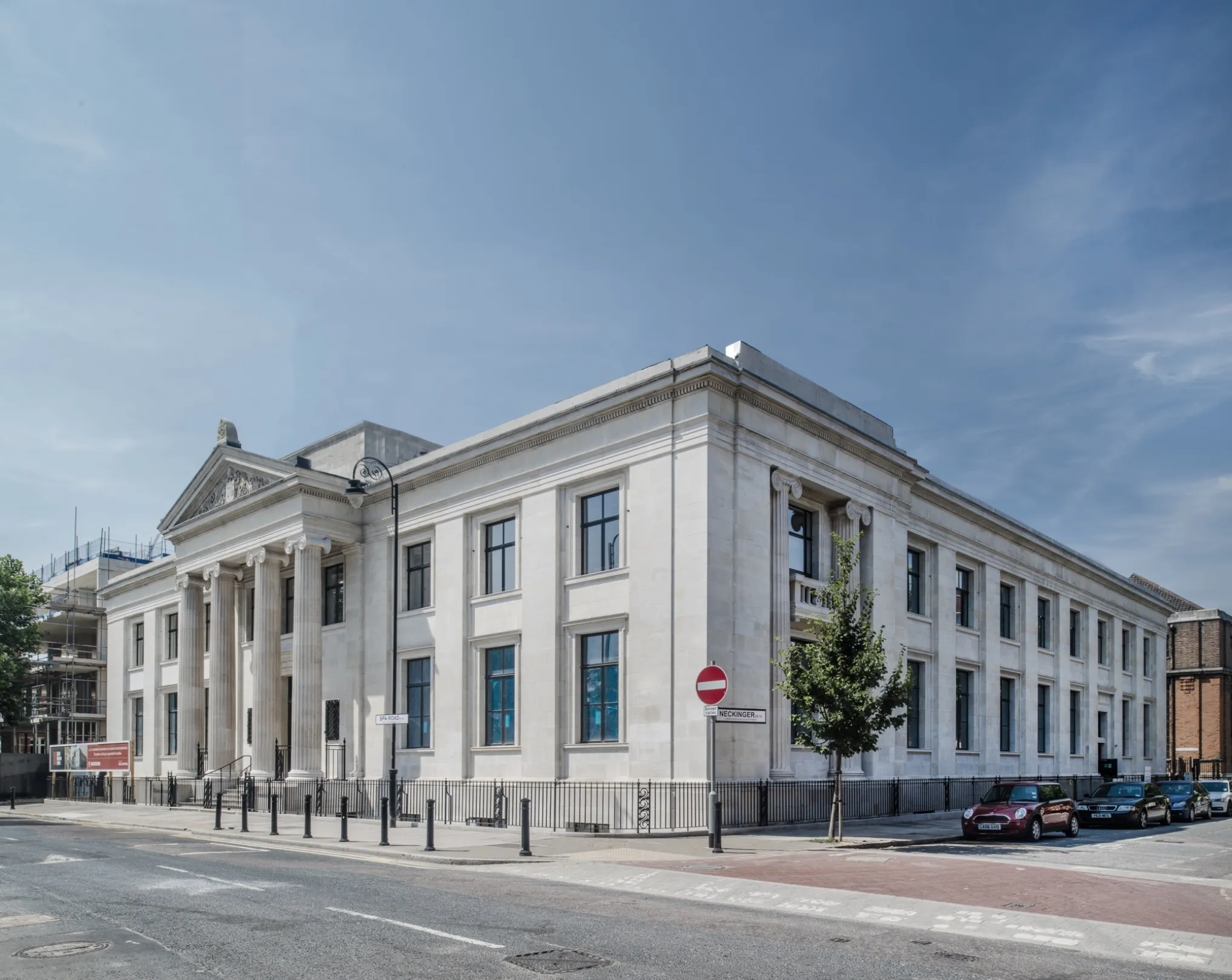 A imposing white building in the Italianate style with four columns supporting a triangular pediment with tympanum above the entrance. Cars are parked down one side.